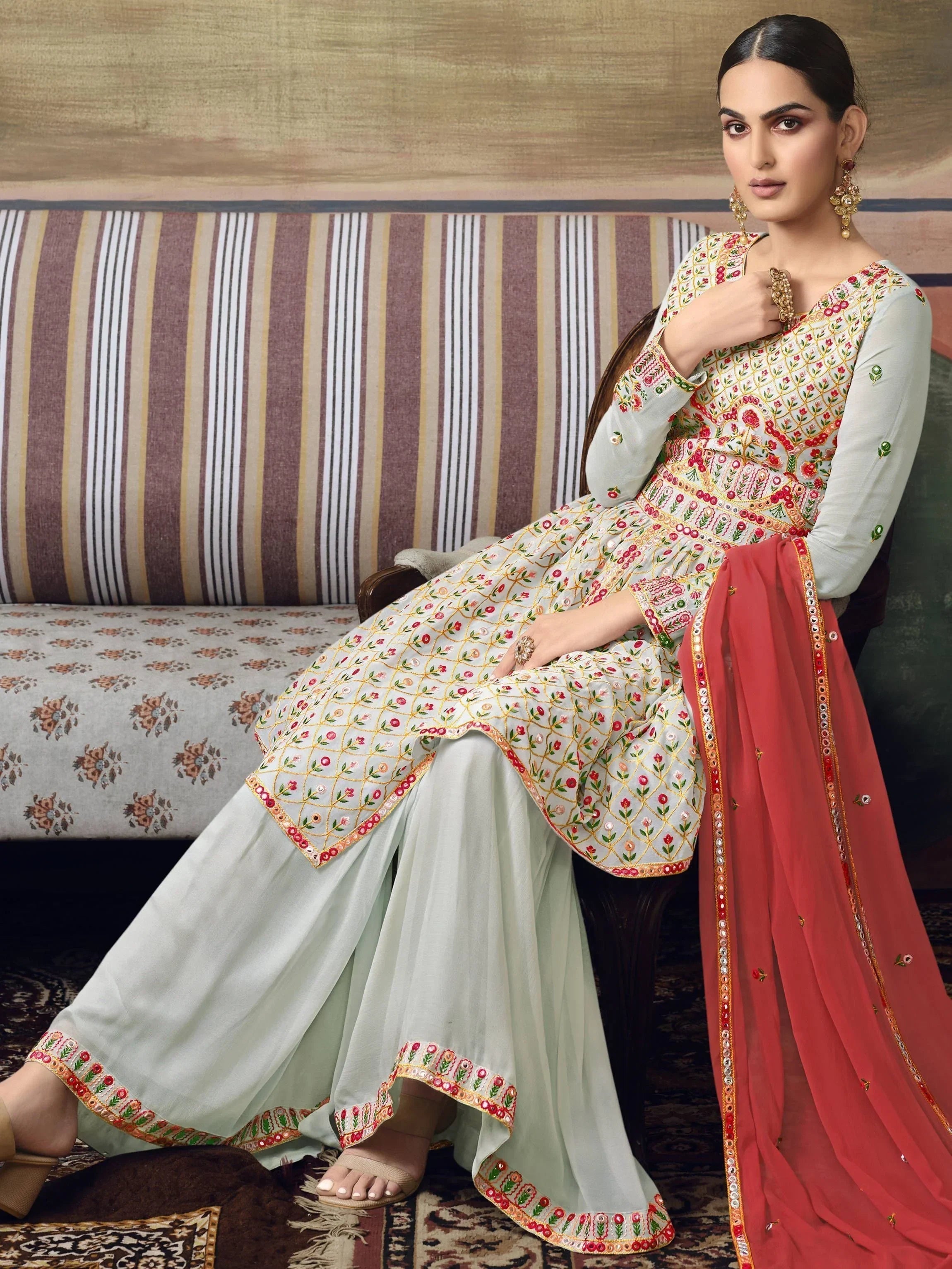 Woman in embroidered Indian salwar kameez with red dupatta sitting on sofa