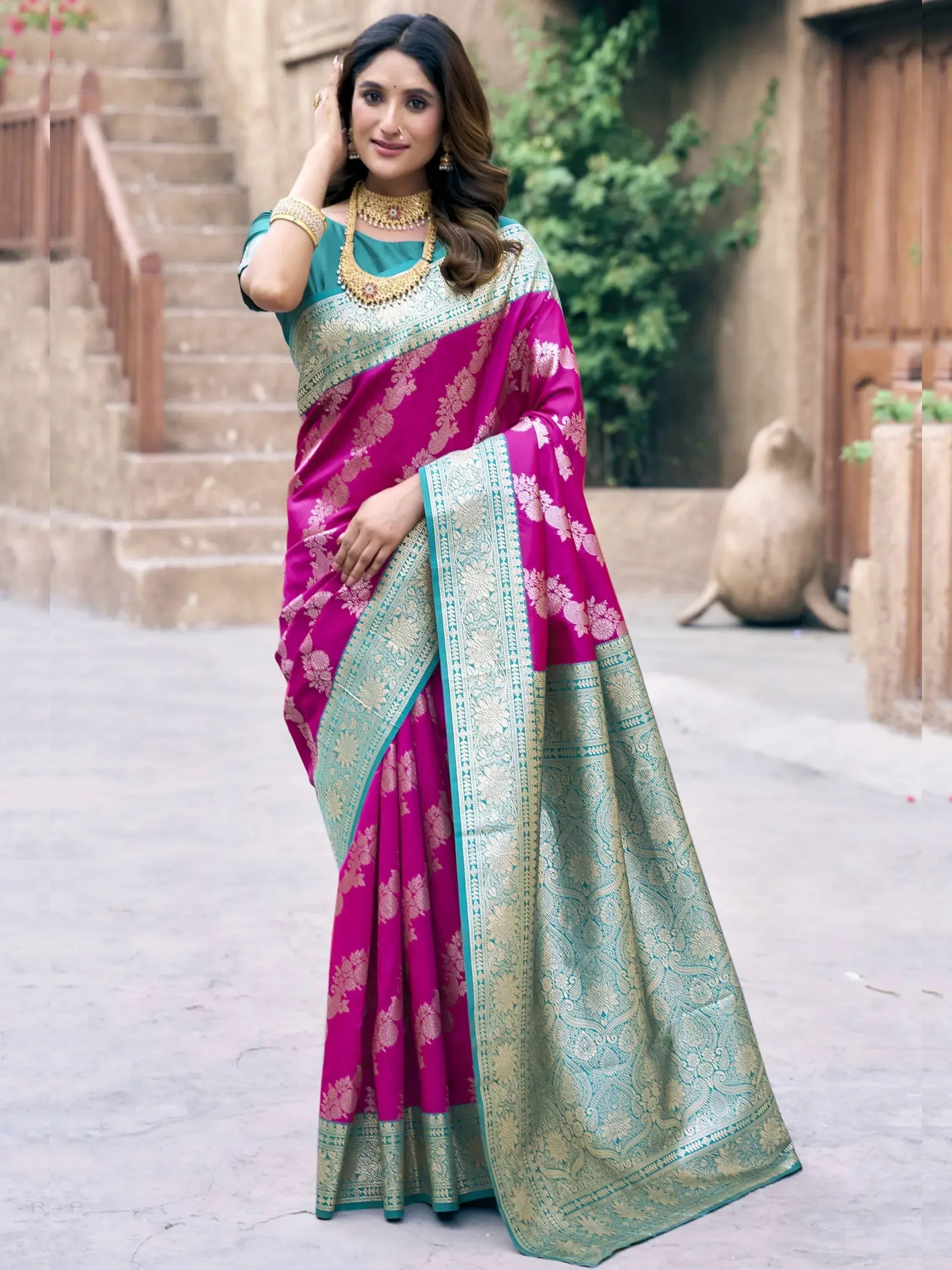 Woman in vibrant pink and teal designer saree with gold embroidery, styled for ethnic occasions