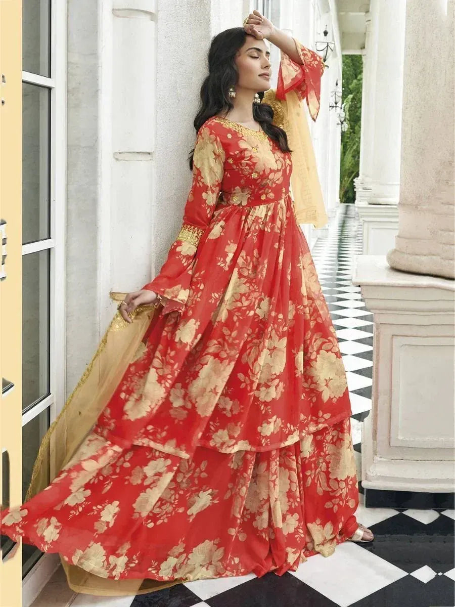 Woman wearing a red and gold floral ethnic gown with dupatta, standing by white pillars