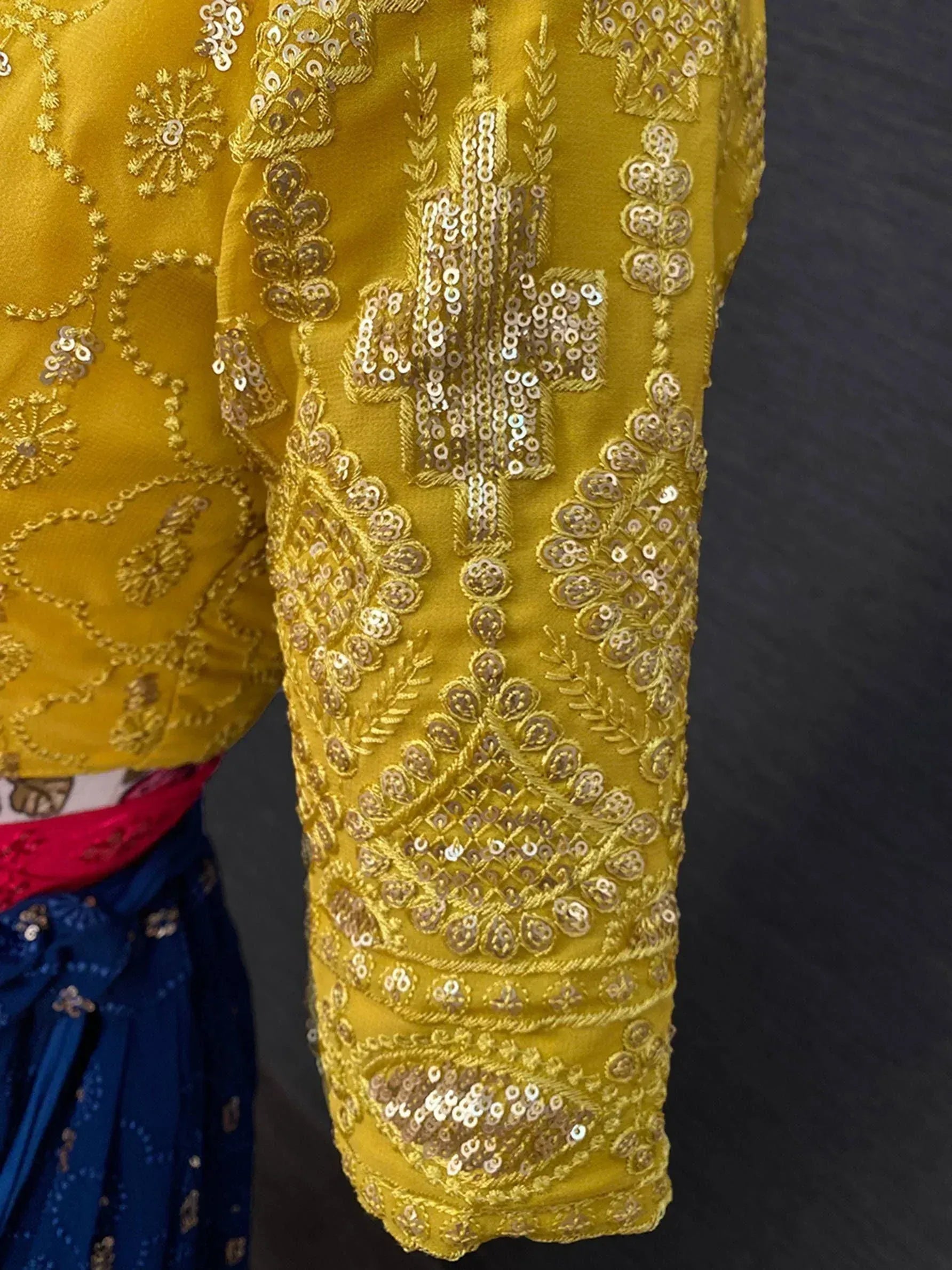 Yellow ethnic blouse with intricate gold embroidery and sequin work, paired with blue lehenga.