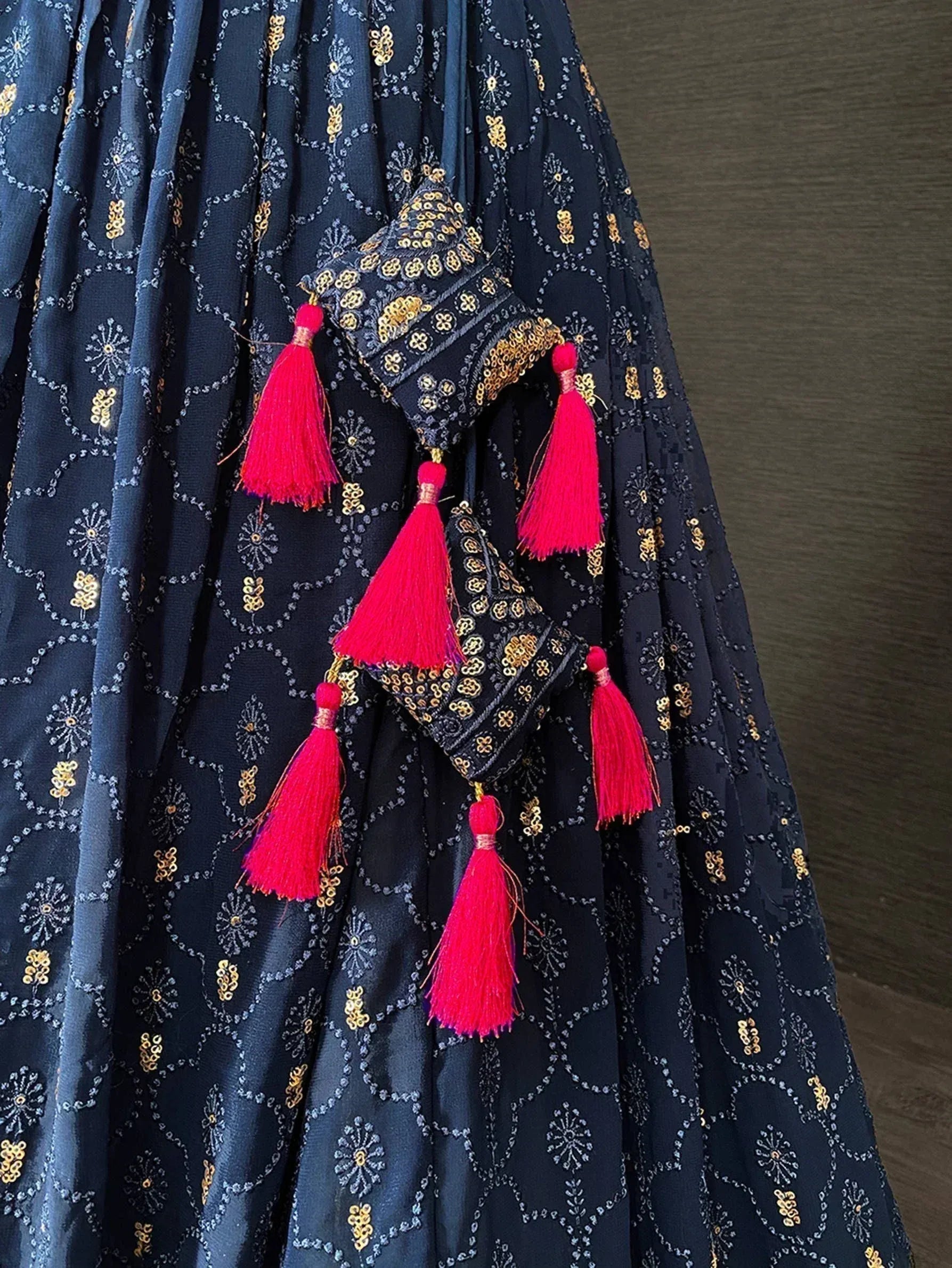 Dark blue ethnic gown with gold embroidery and pink tassels, perfect for Indian festive occasions.