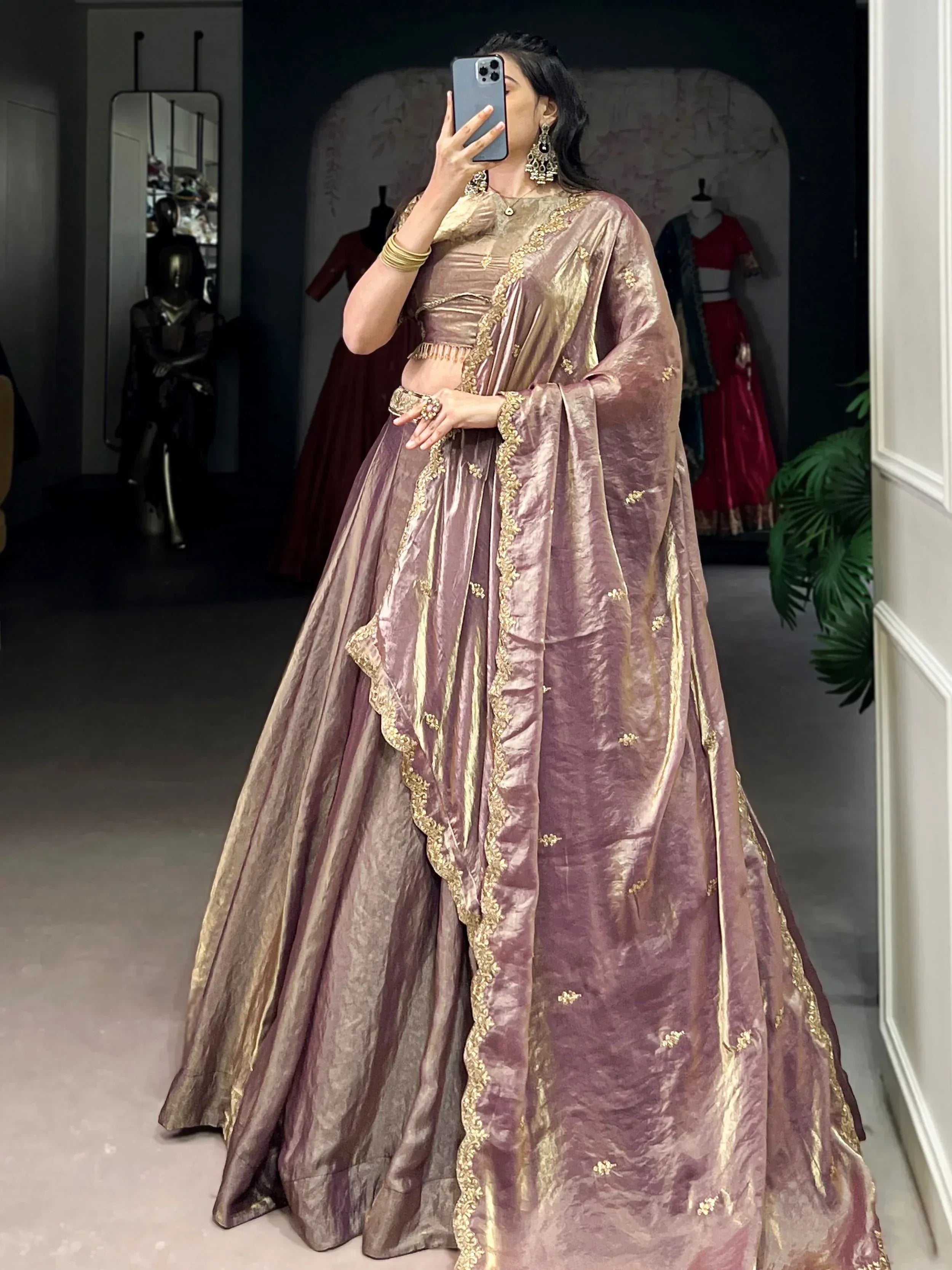 Woman in mauve velvet lehenga choli with gold embroidery, taking mirror selfie in boutique