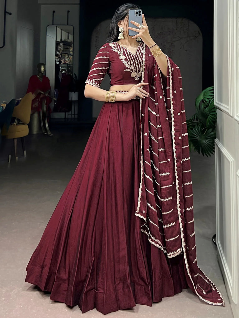 Woman wearing a maroon designer lehenga choli with intricate white embroidery and matching dupatta.