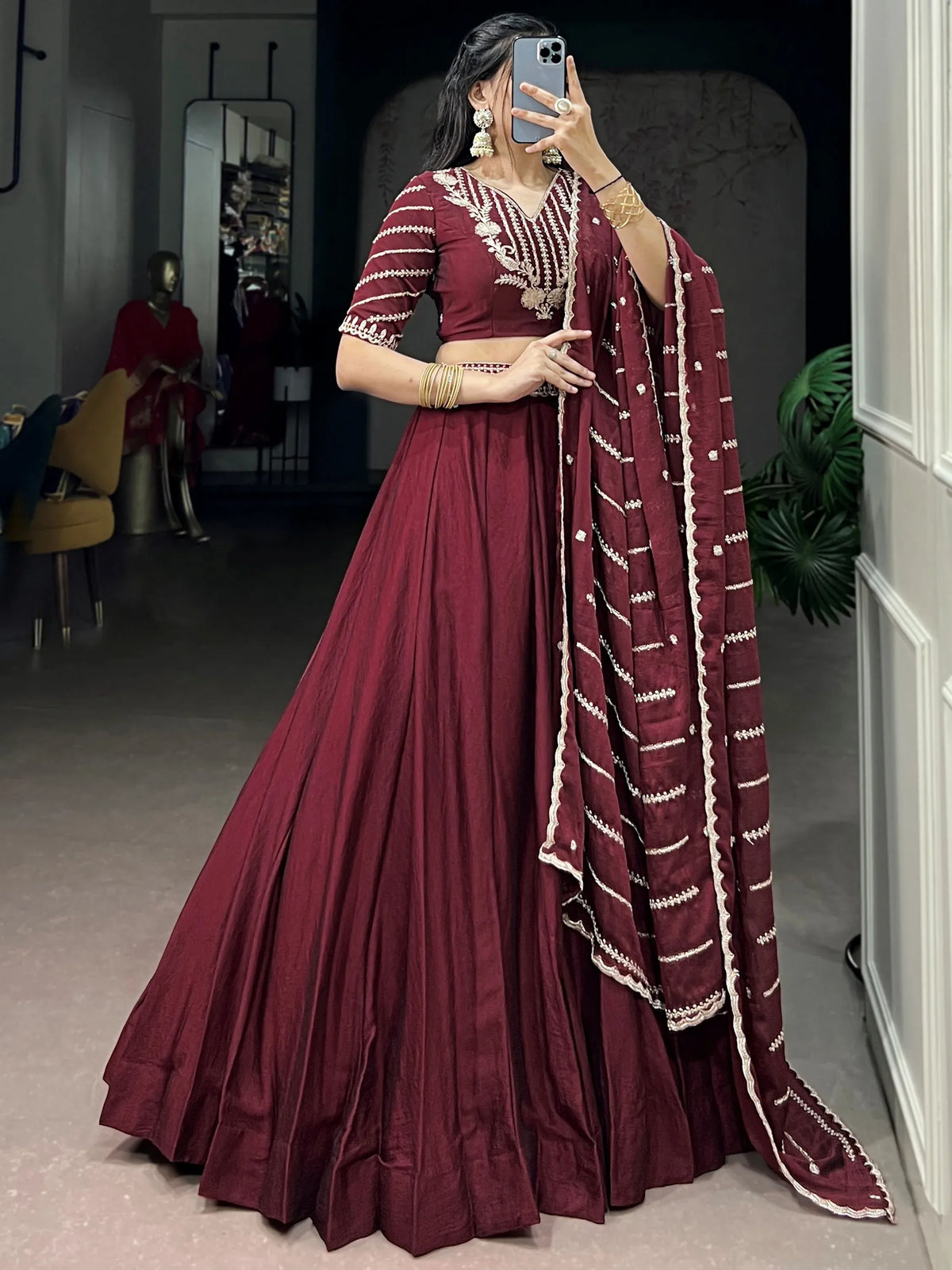 Woman wearing a maroon designer lehenga choli with intricate white embroidery and matching dupatta.