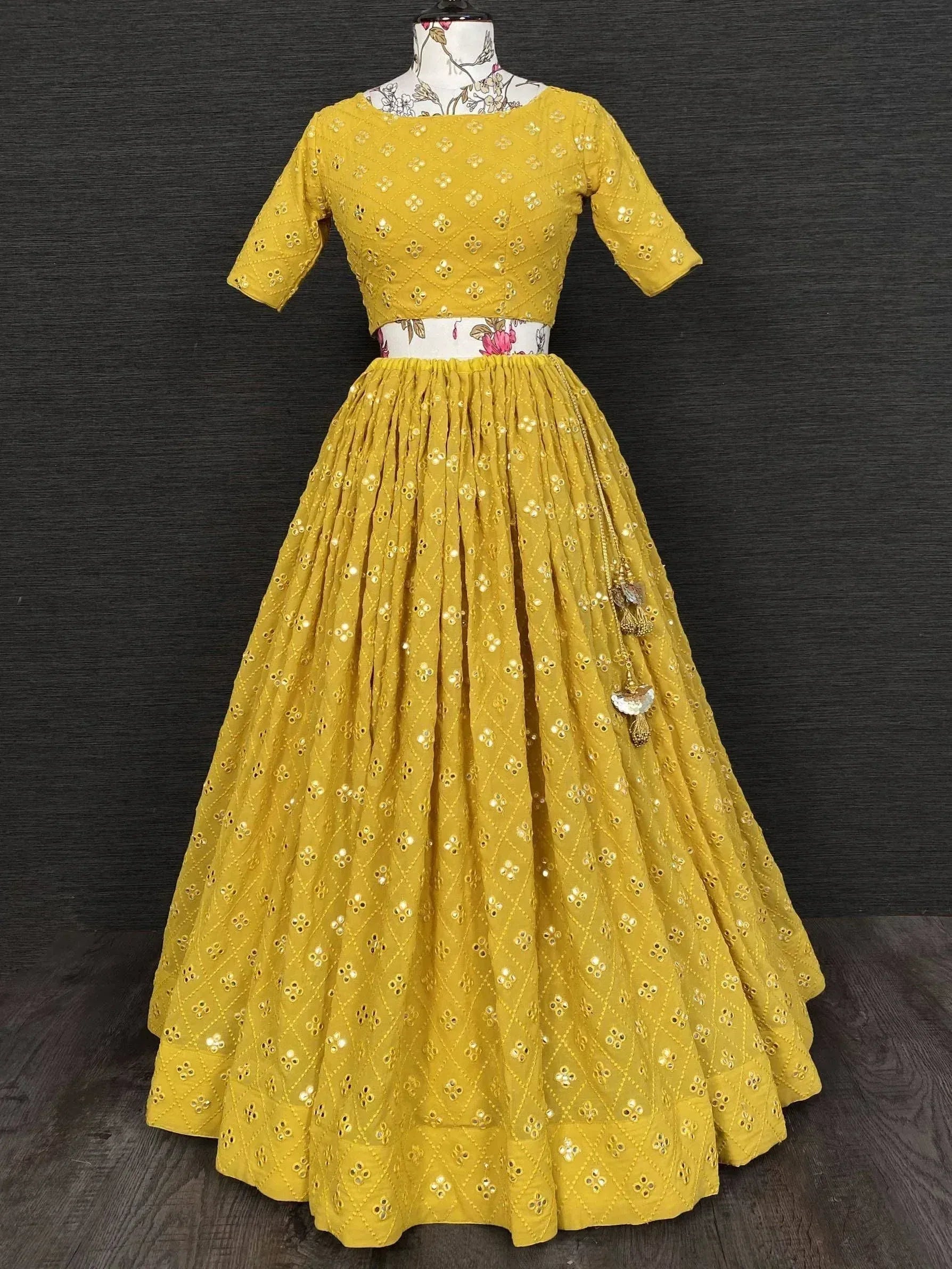 Yellow ethnic lehenga choli with mirror work and floral belt, perfect for Indian weddings and festive occasions.