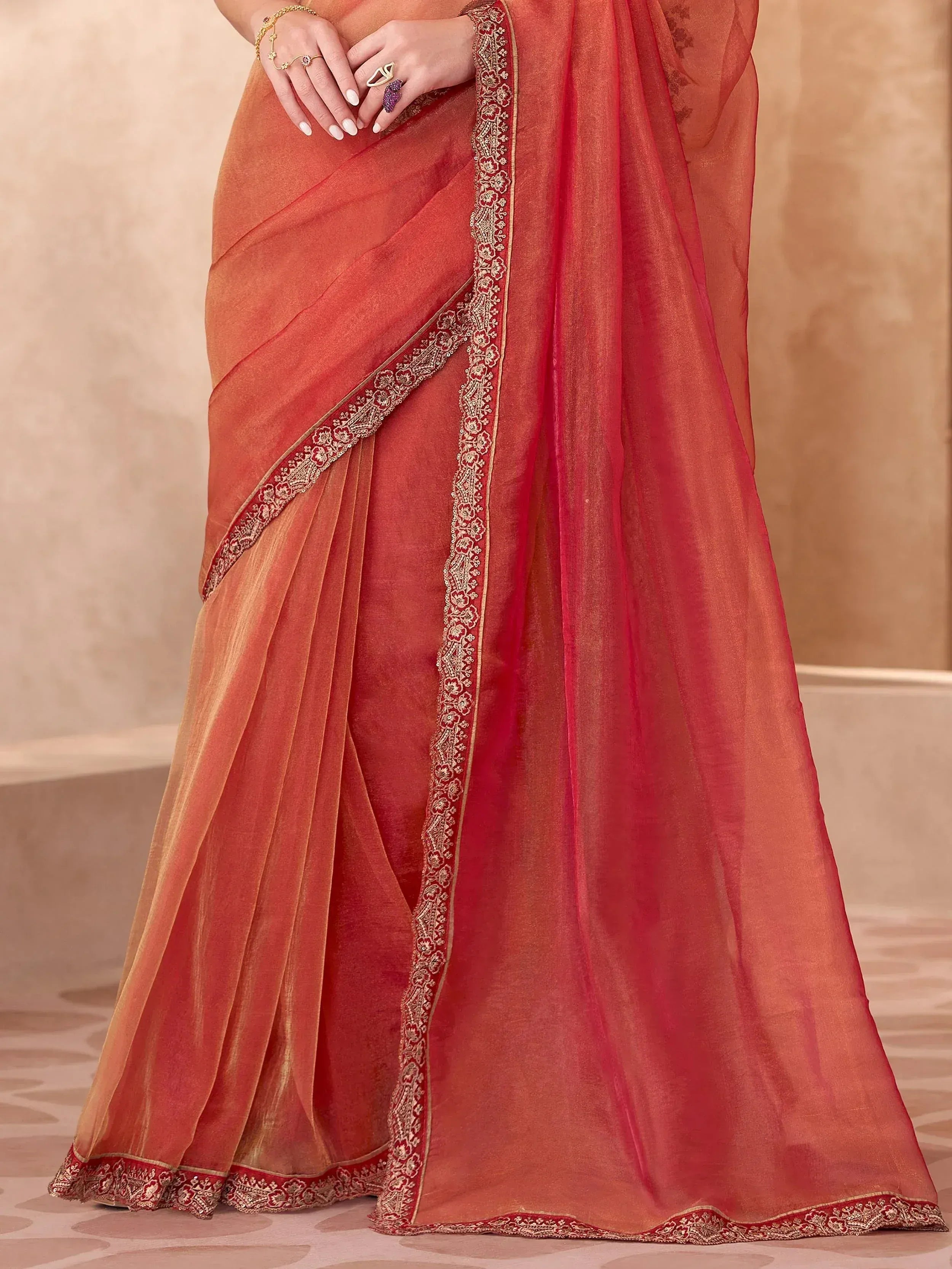 Elegant coral saree with intricate gold embroidery and border detailing, perfect for ethnic occasions.