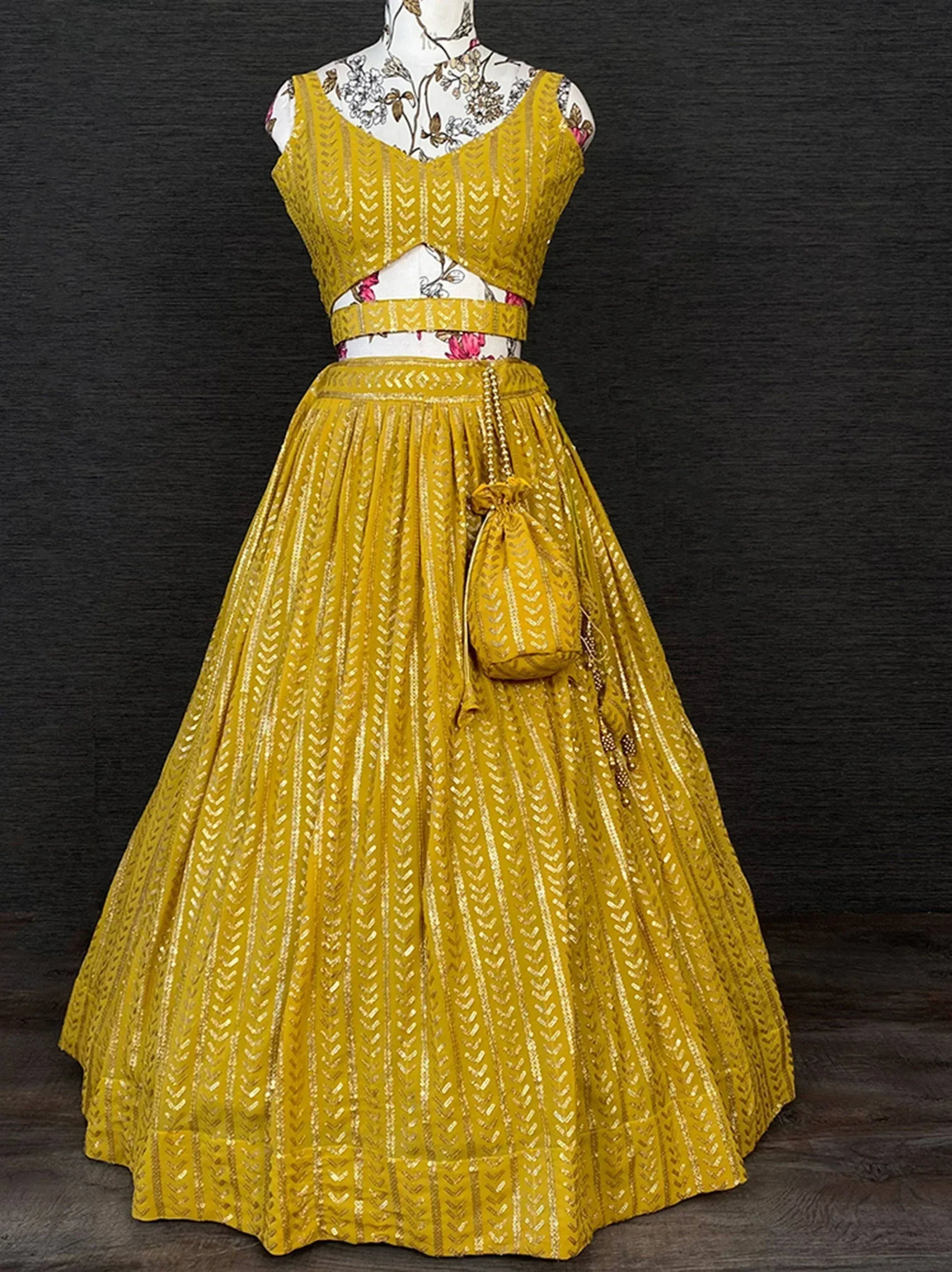 Mustard yellow designer lehenga choli with gold embroidery, pleated skirt, and matching potli bag for Indian ethnic wear