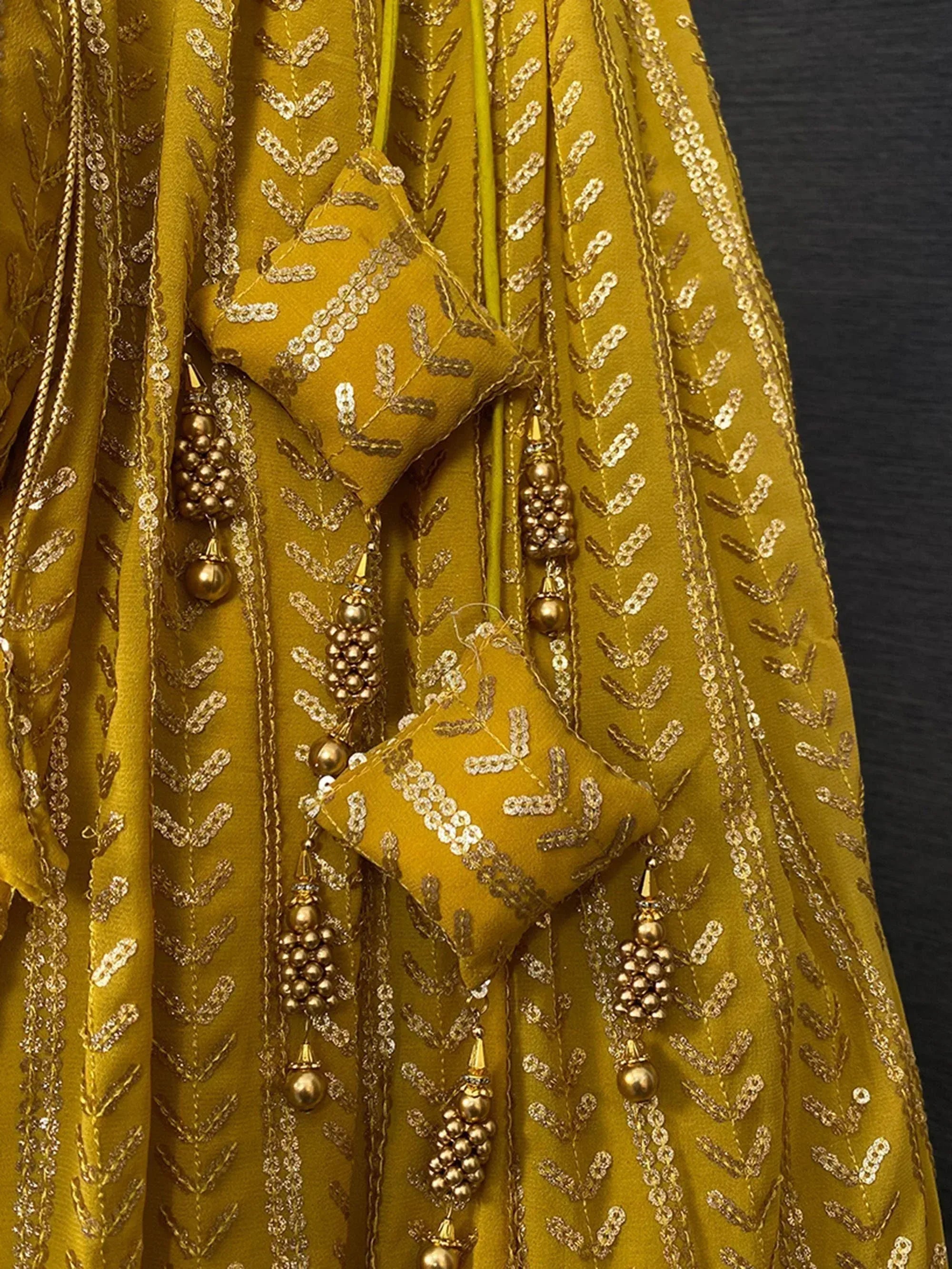 Mustard yellow ethnic lehenga with gold embroidery and bead tassels, perfect for Indian weddings and festive occasions.