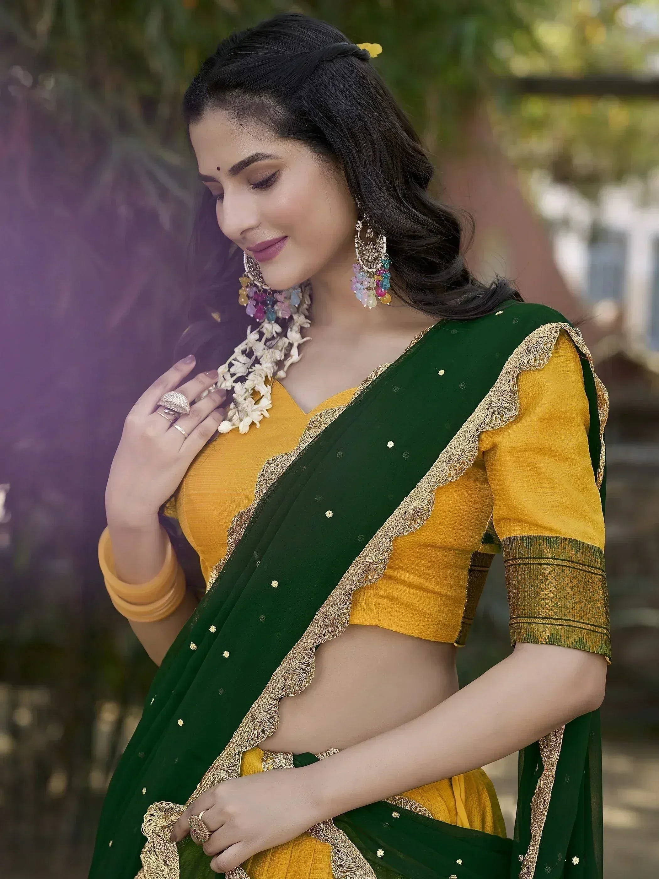 Woman in green and yellow saree with gold embroidery, floral garland, and colorful earrings for ethnic wear