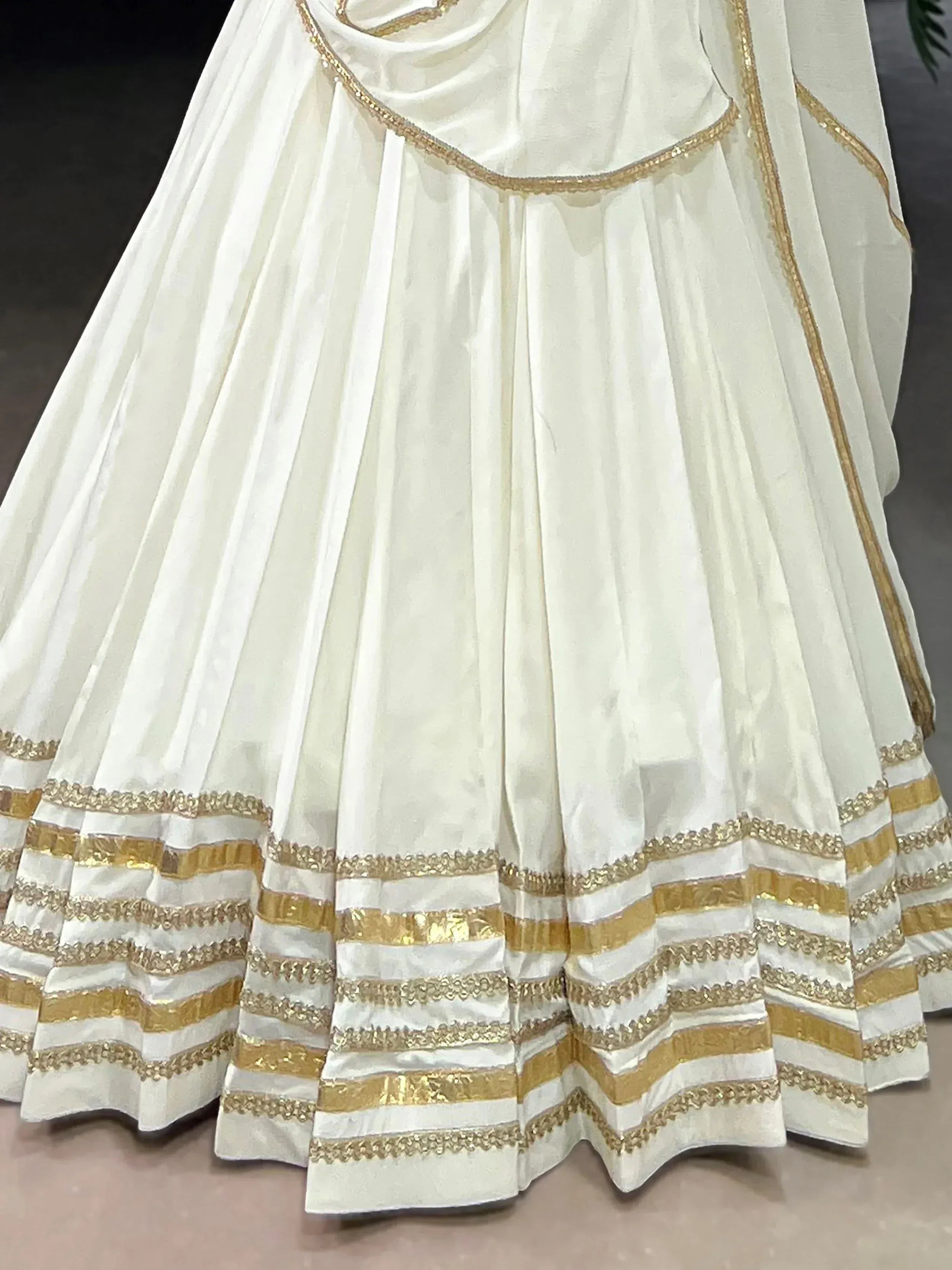 White ethnic lehenga with gold trim and pleated skirt, perfect for Indian weddings and festive occasions