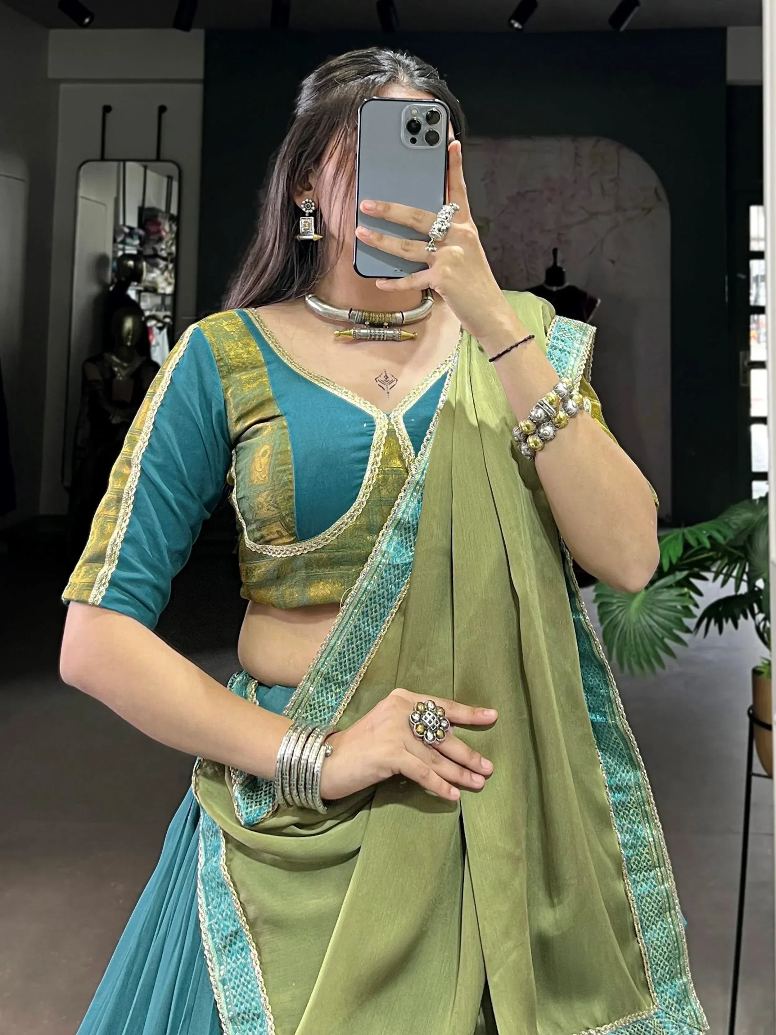Woman in green and teal ethnic lehenga choli with gold embroidery, mirror selfie in boutique