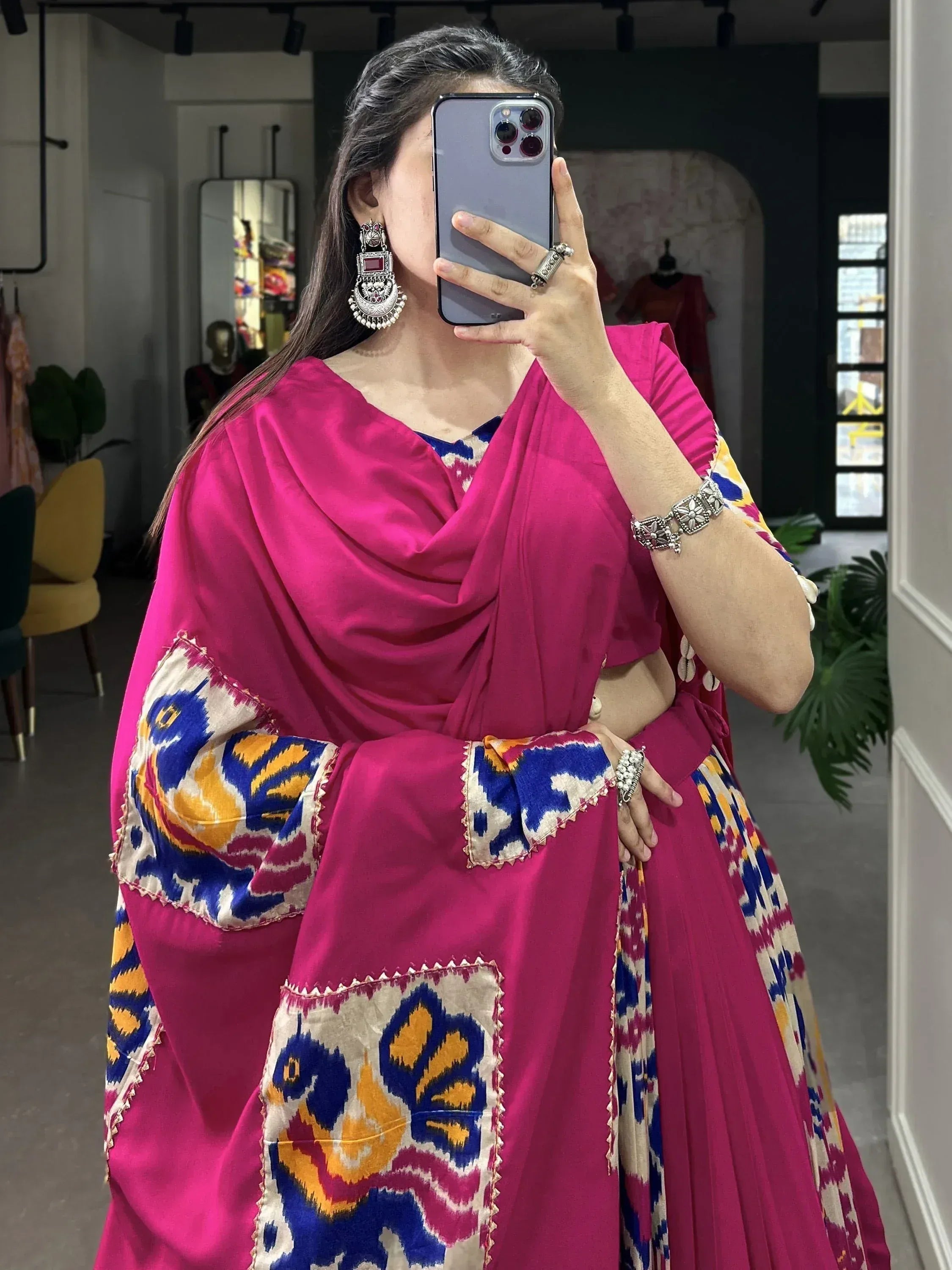 Woman in vibrant pink ethnic lehenga with ikat print, styled with statement jewelry for festive occasions.