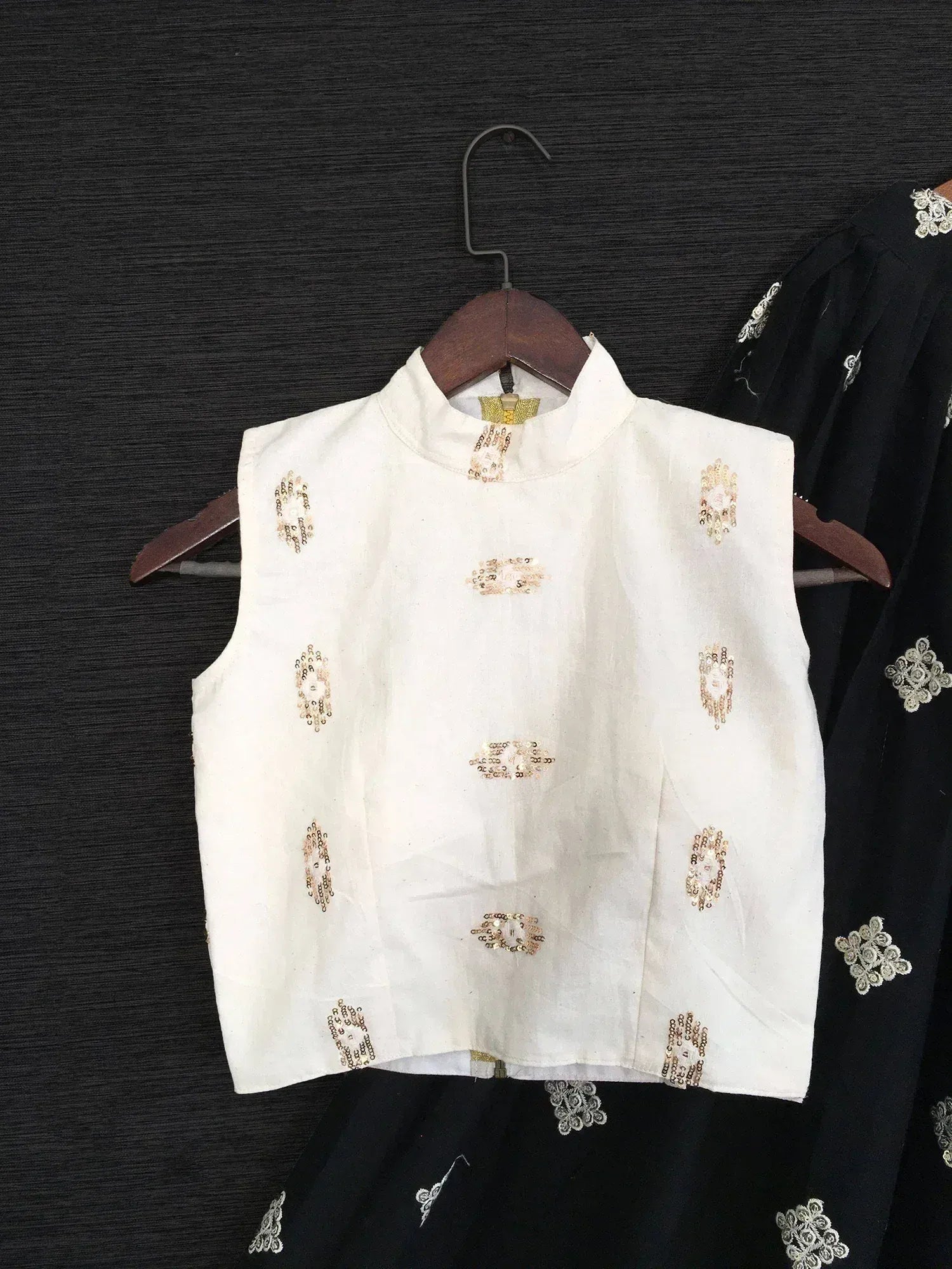 White sleeveless ethnic blouse with gold sequin embroidery, paired with black embroidered skirt