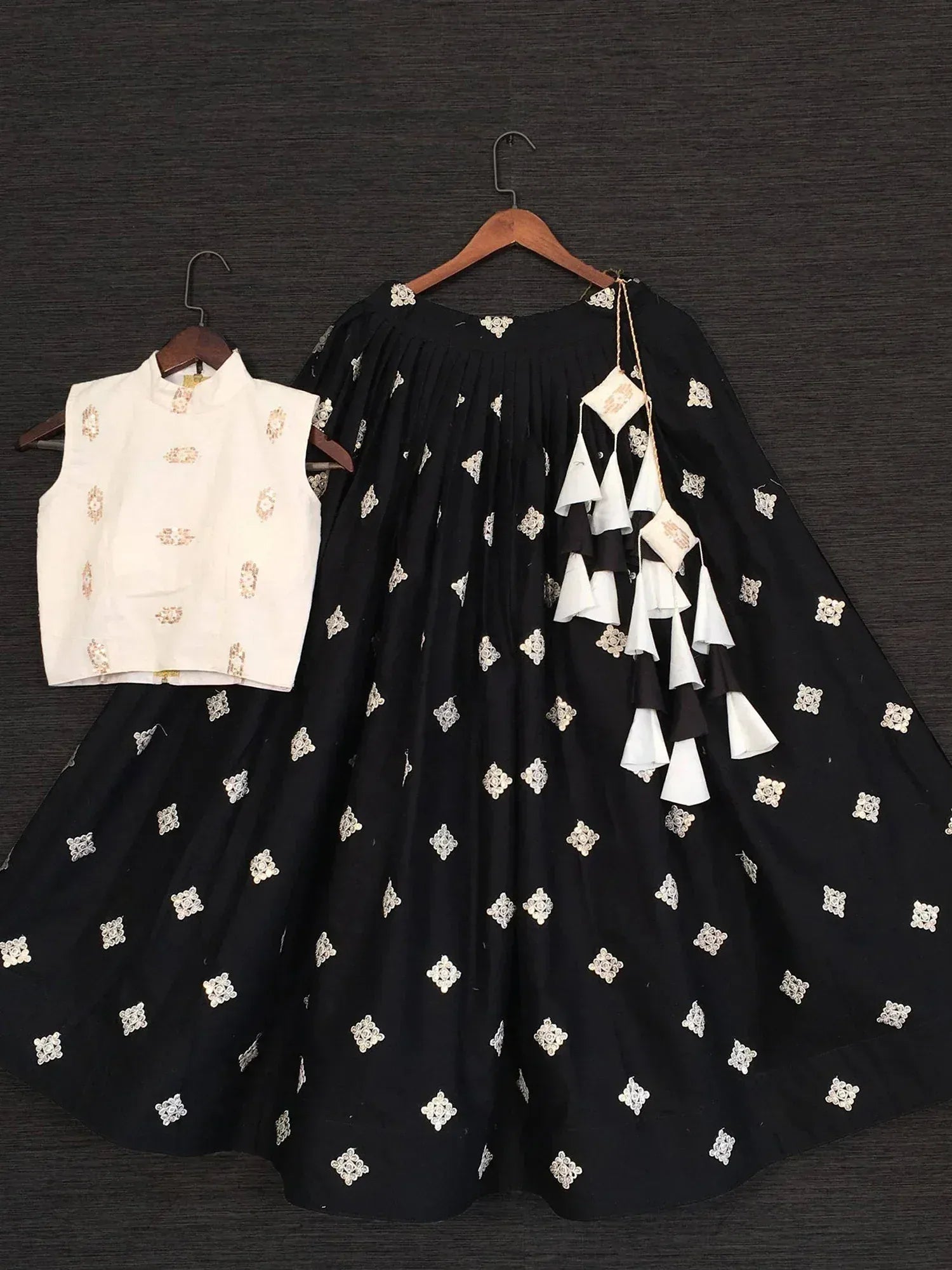 Black embroidered lehenga with white floral motifs and tassels, paired with white sleeveless blouse