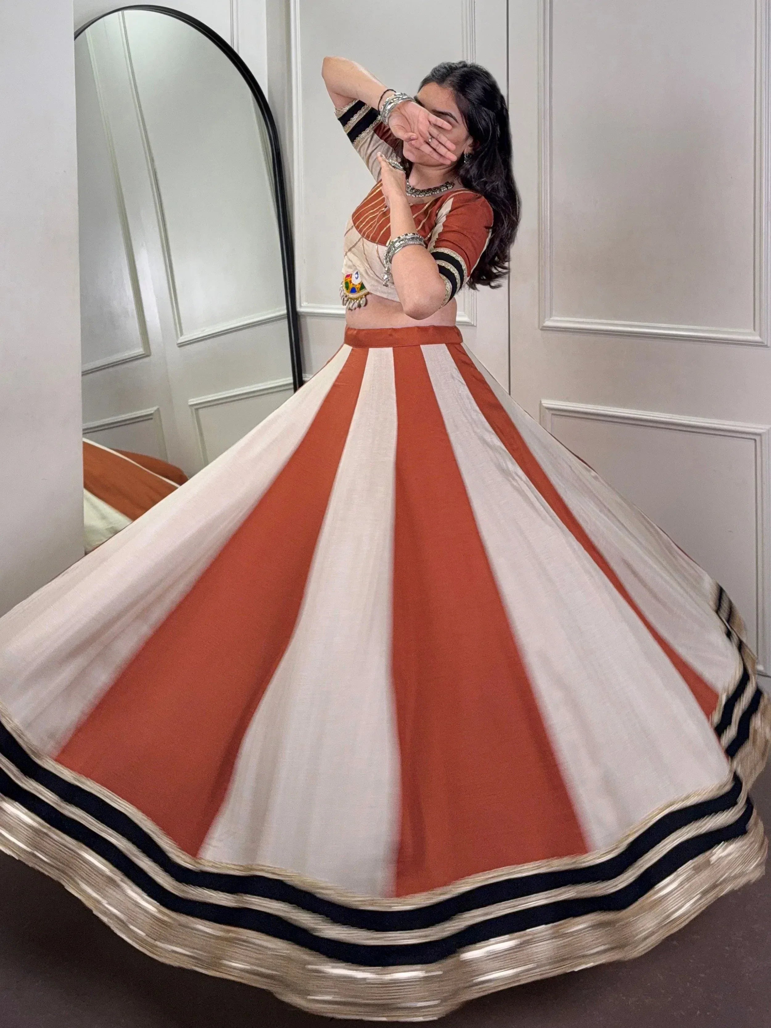 Woman twirling in orange and white striped lehenga choli with mirror backdrop, ethnic Indian wear