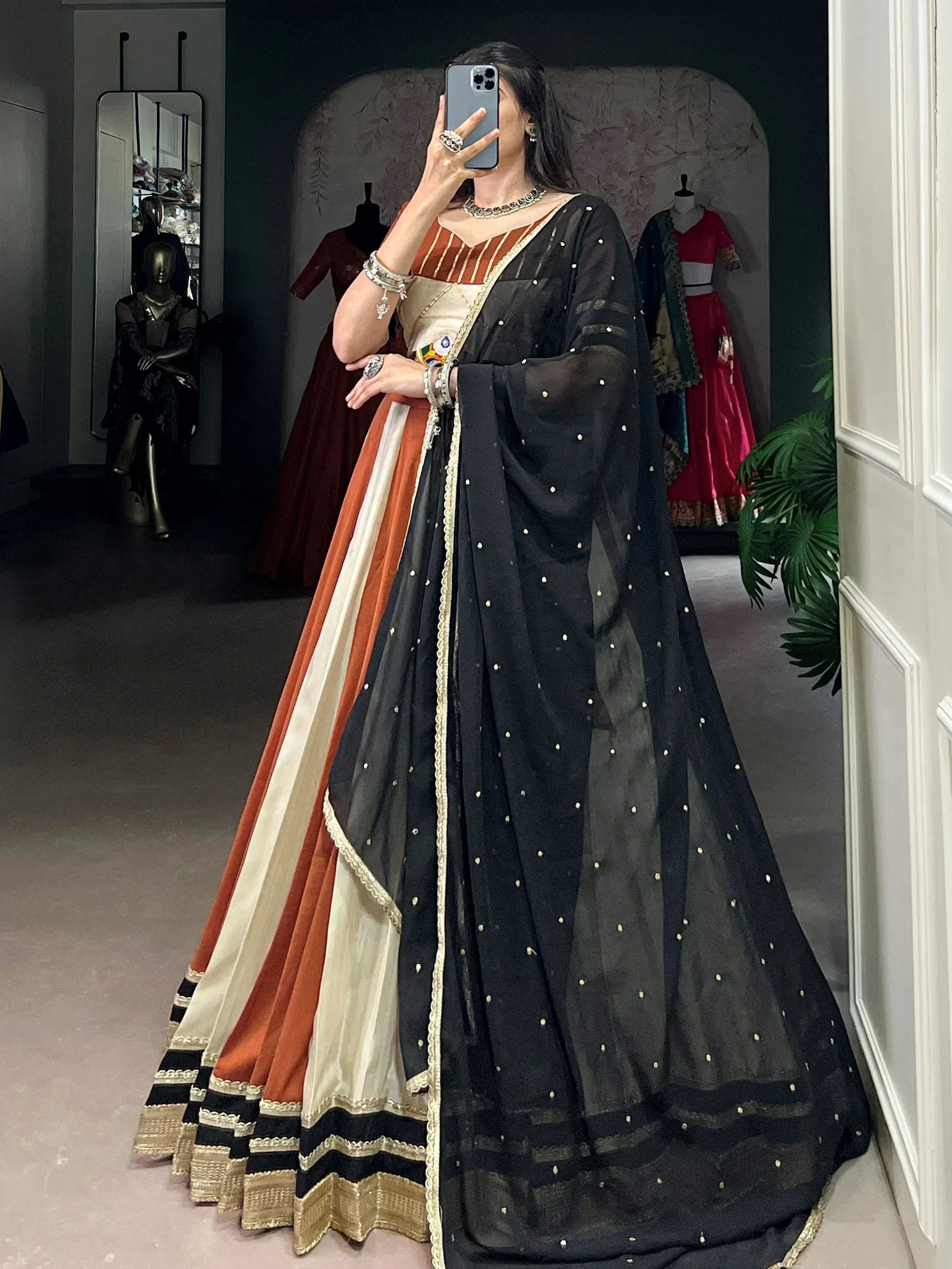 Woman in black sheer dupatta with gold dots, orange and cream lehenga choli, ethnic Indian wear