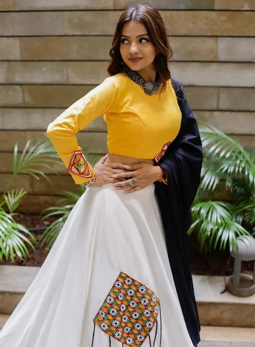 Yellow crop top with embroidered sleeves paired with white lehenga featuring floral patchwork, styled with black dupatta for ethnic wear