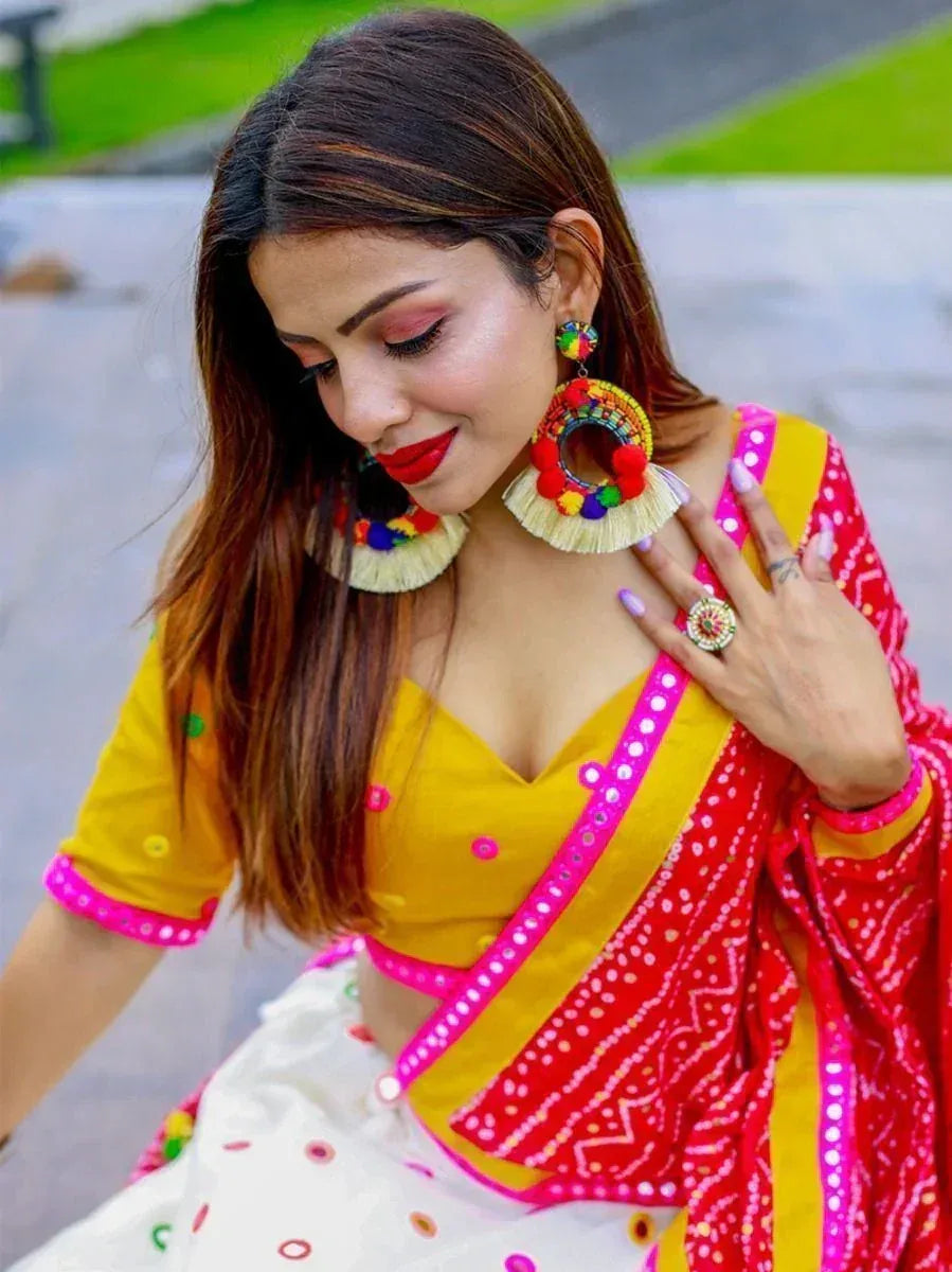 Woman in vibrant yellow and red ethnic lehenga choli with colorful mirror work and pom-pom earrings