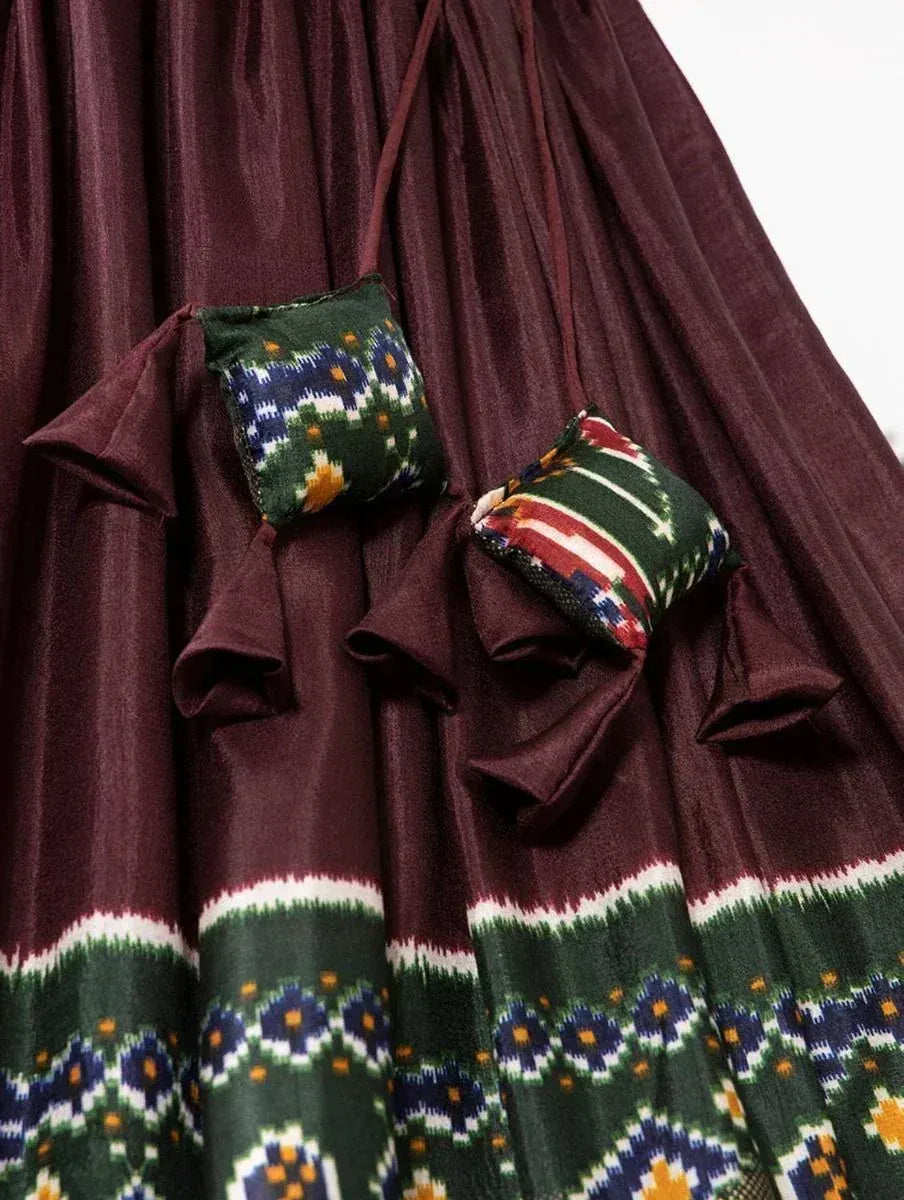 Maroon ethnic gown with green ikat print and matching decorative pouches, perfect for festive occasions.