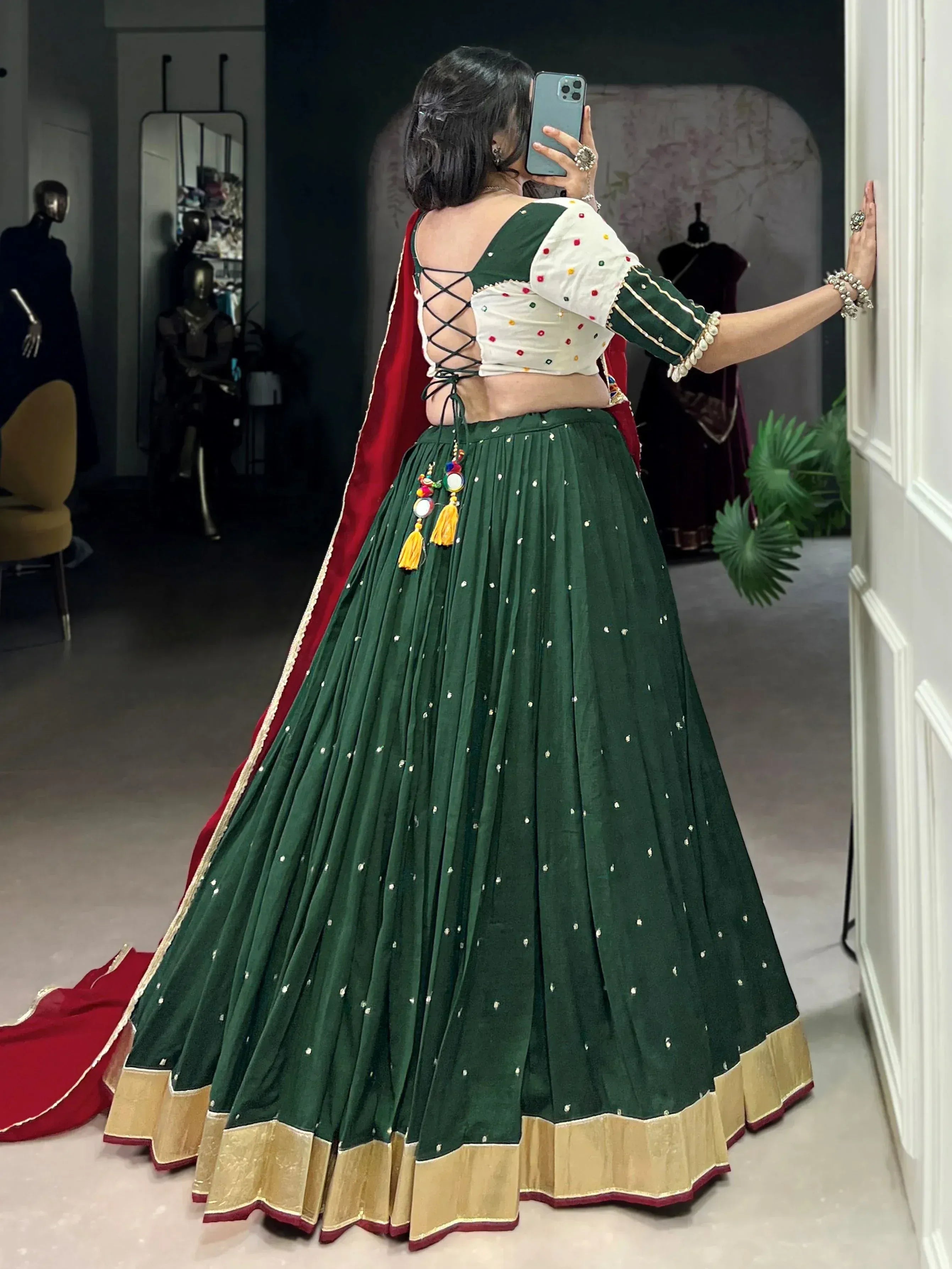 Green and red ethnic lehenga choli with mirror work, lace-up back, and gold trim, perfect for Indian weddings or festive occasions.