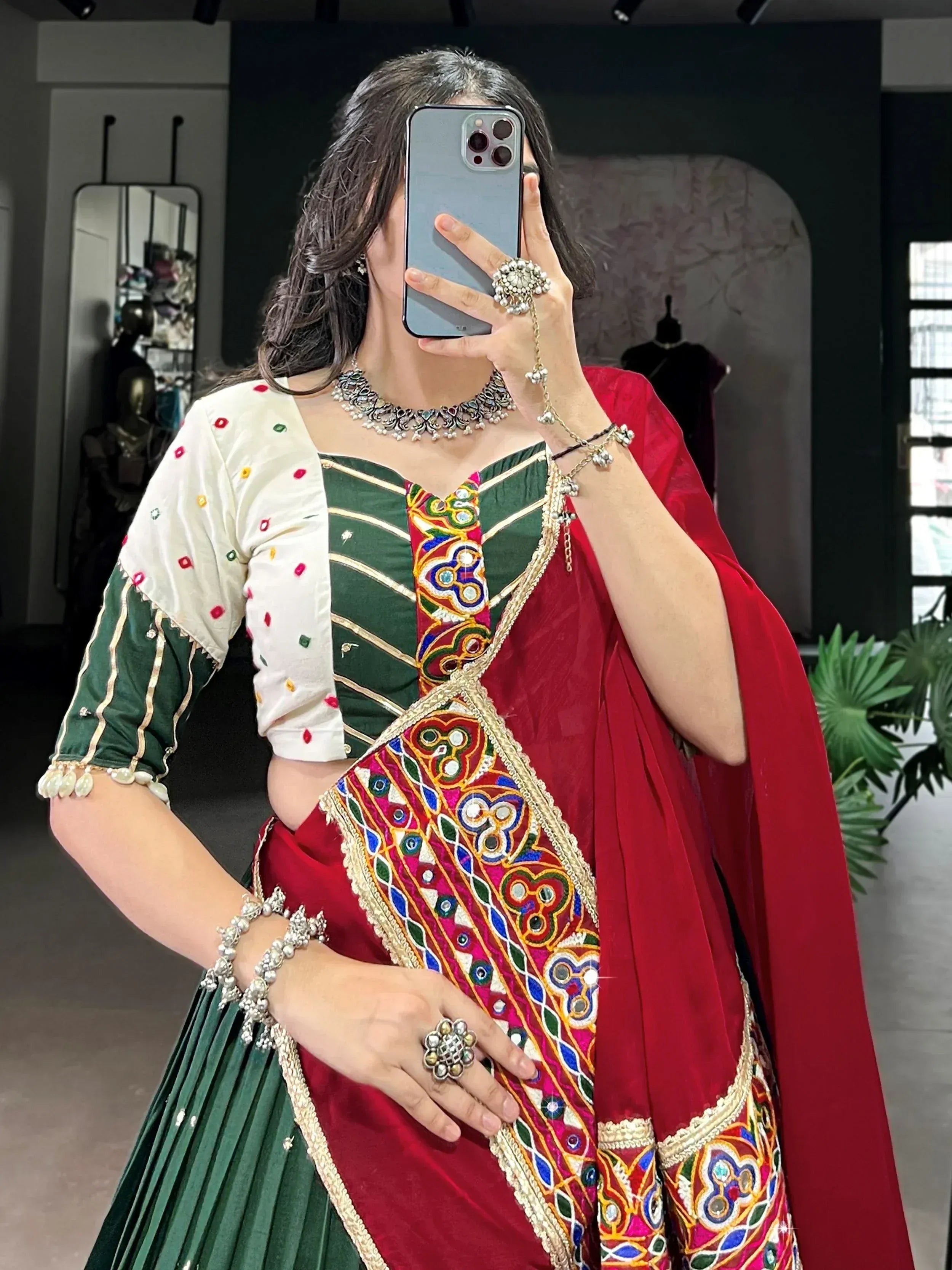 Woman in green and red embroidered Indian ethnic wear with mirror work, traditional jewelry, and dupatta