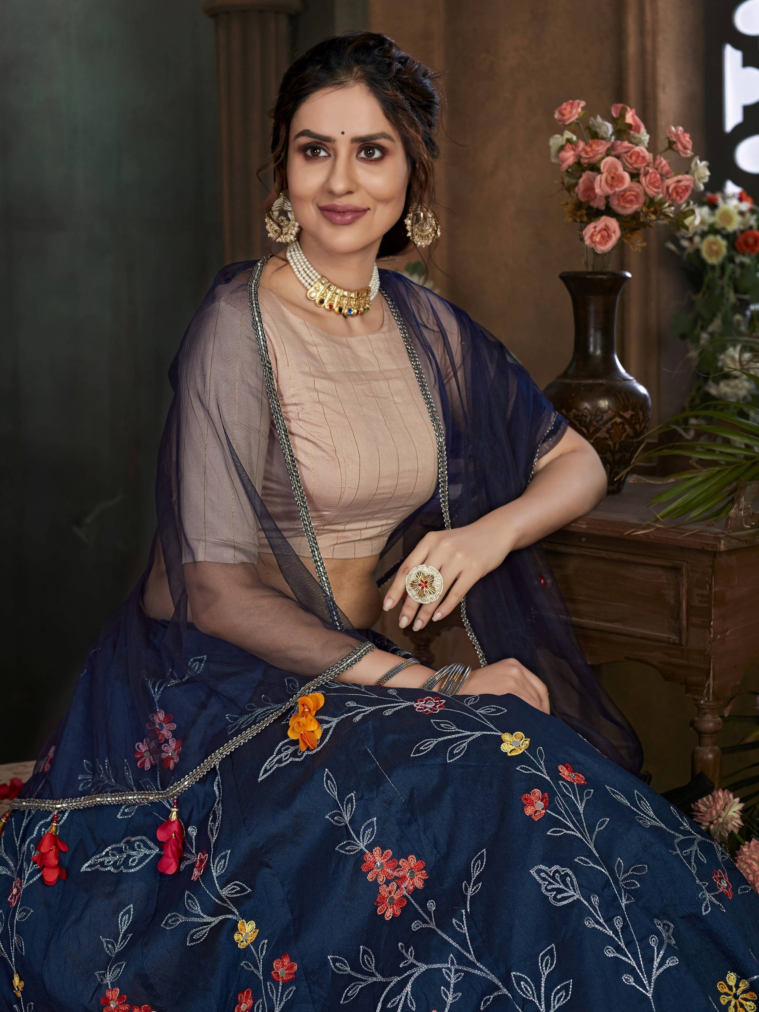 Woman in navy blue embroidered lehenga choli with floral detailing and gold jewelry, perfect for Indian ethnic wear.
