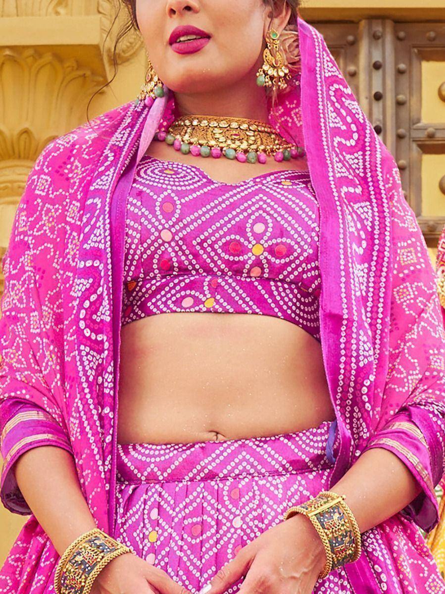 Vibrant pink ethnic lehenga choli with mirror work, paired with gold jewelry and dupatta, perfect for Indian celebrations.