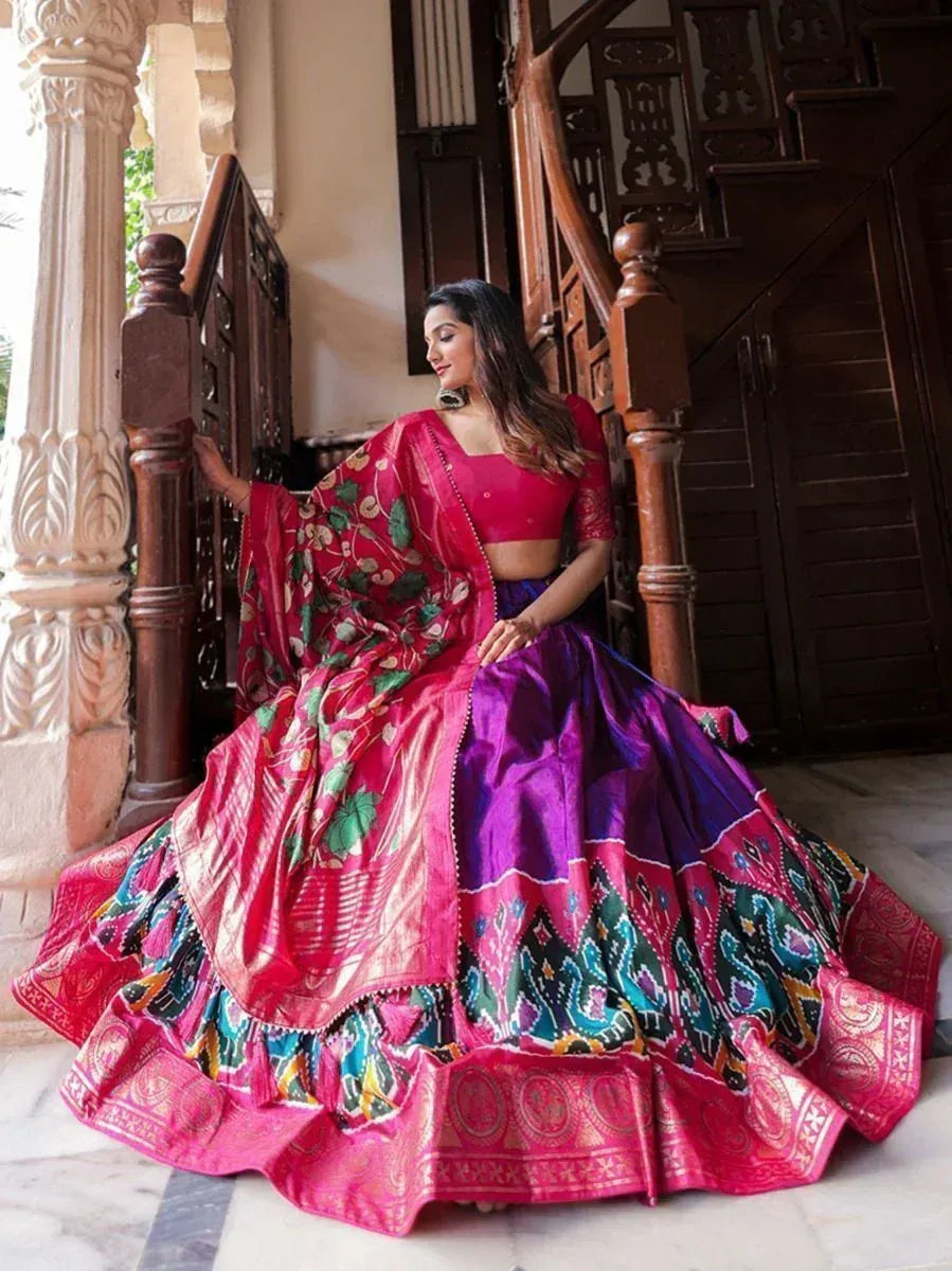 Woman in vibrant pink and purple designer lehenga choli with floral dupatta, posing on ornate staircase