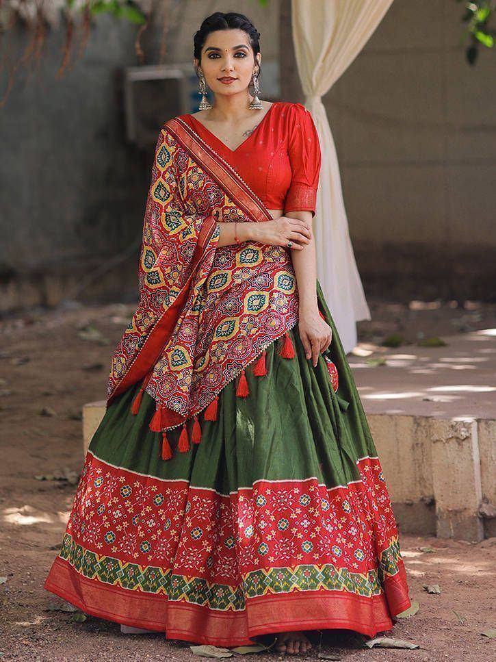Woman in red and green ethnic lehenga choli with printed dupatta and tassels, perfect for Indian weddings or festivals.