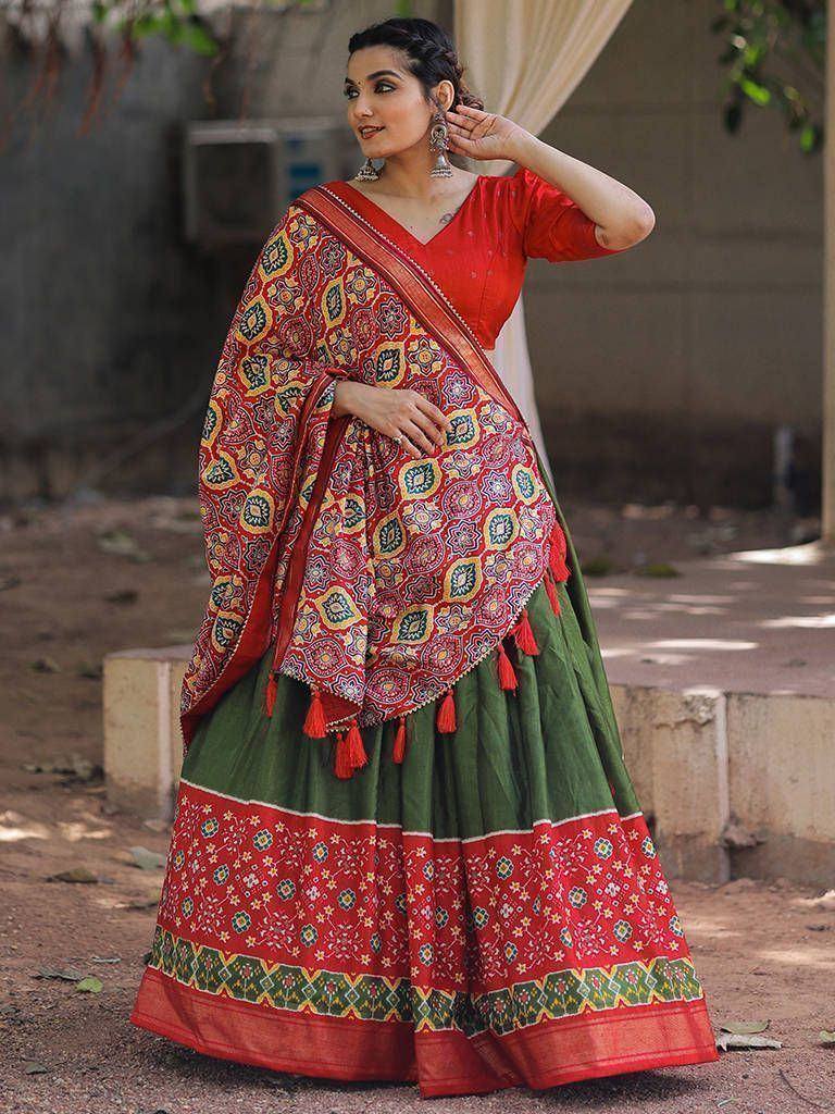 Woman in vibrant red and green ethnic lehenga choli with floral print and tassels, perfect for festive occasions.