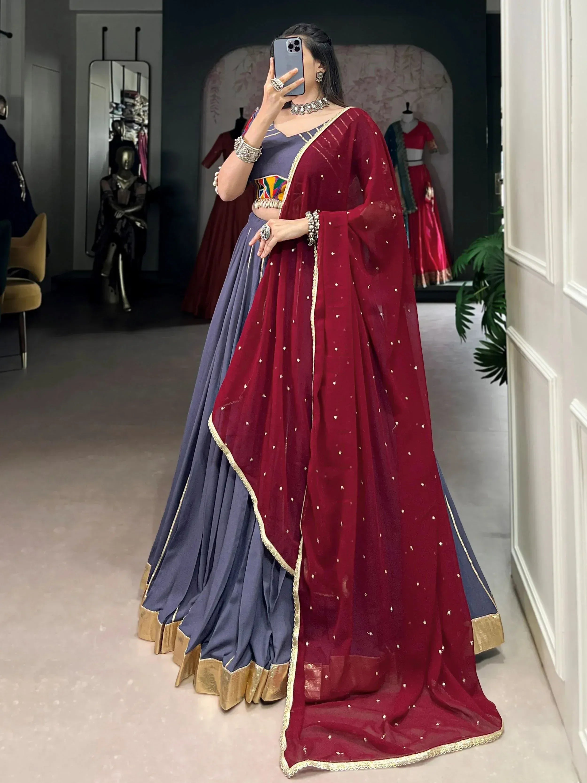 Woman in maroon and blue designer lehenga choli with gold trim and embellished dupatta, perfect for Indian ethnic wear occasions.