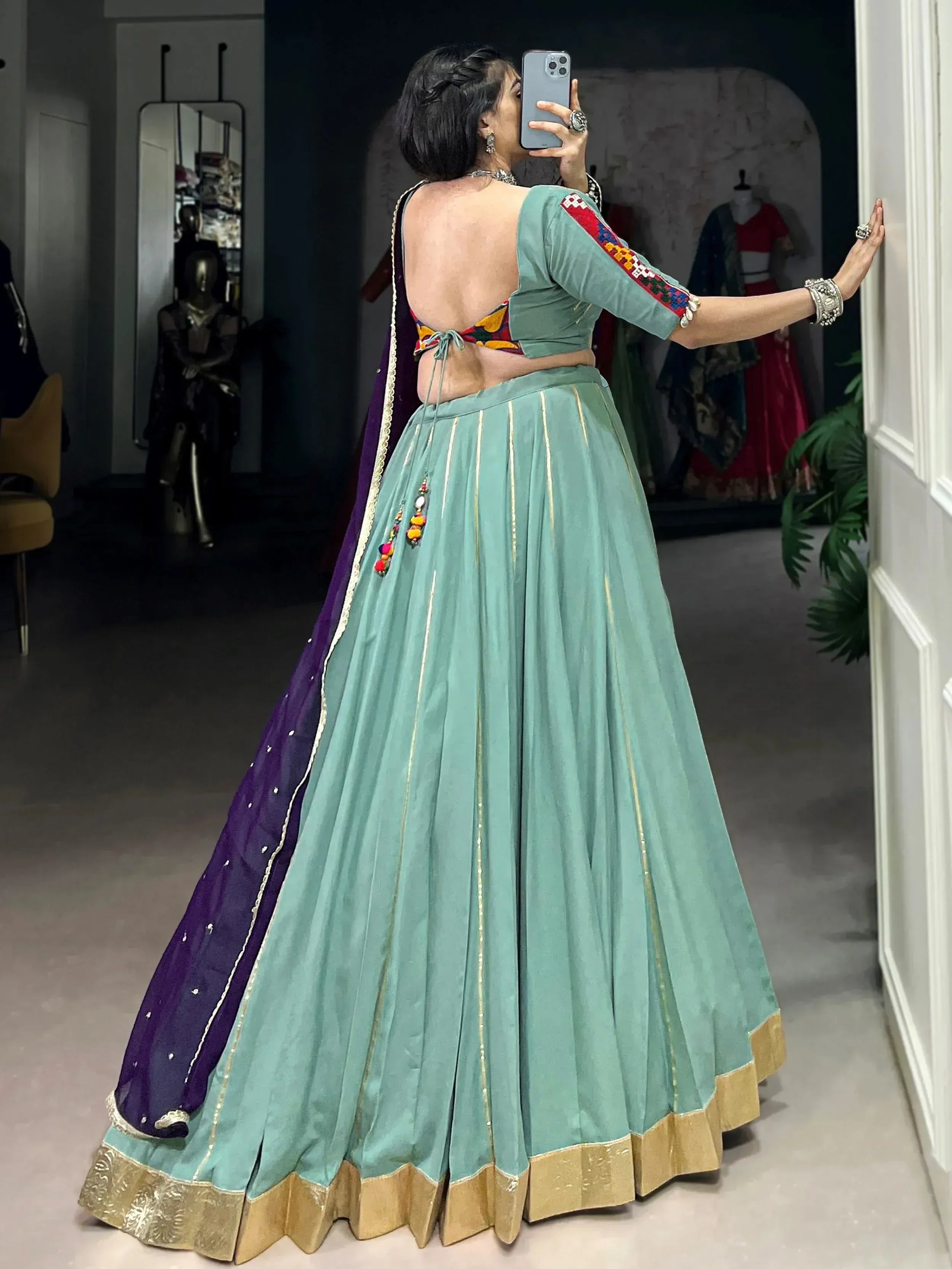Woman taking mirror selfie in mint green lehenga choli with purple dupatta, gold trim, and backless blouse