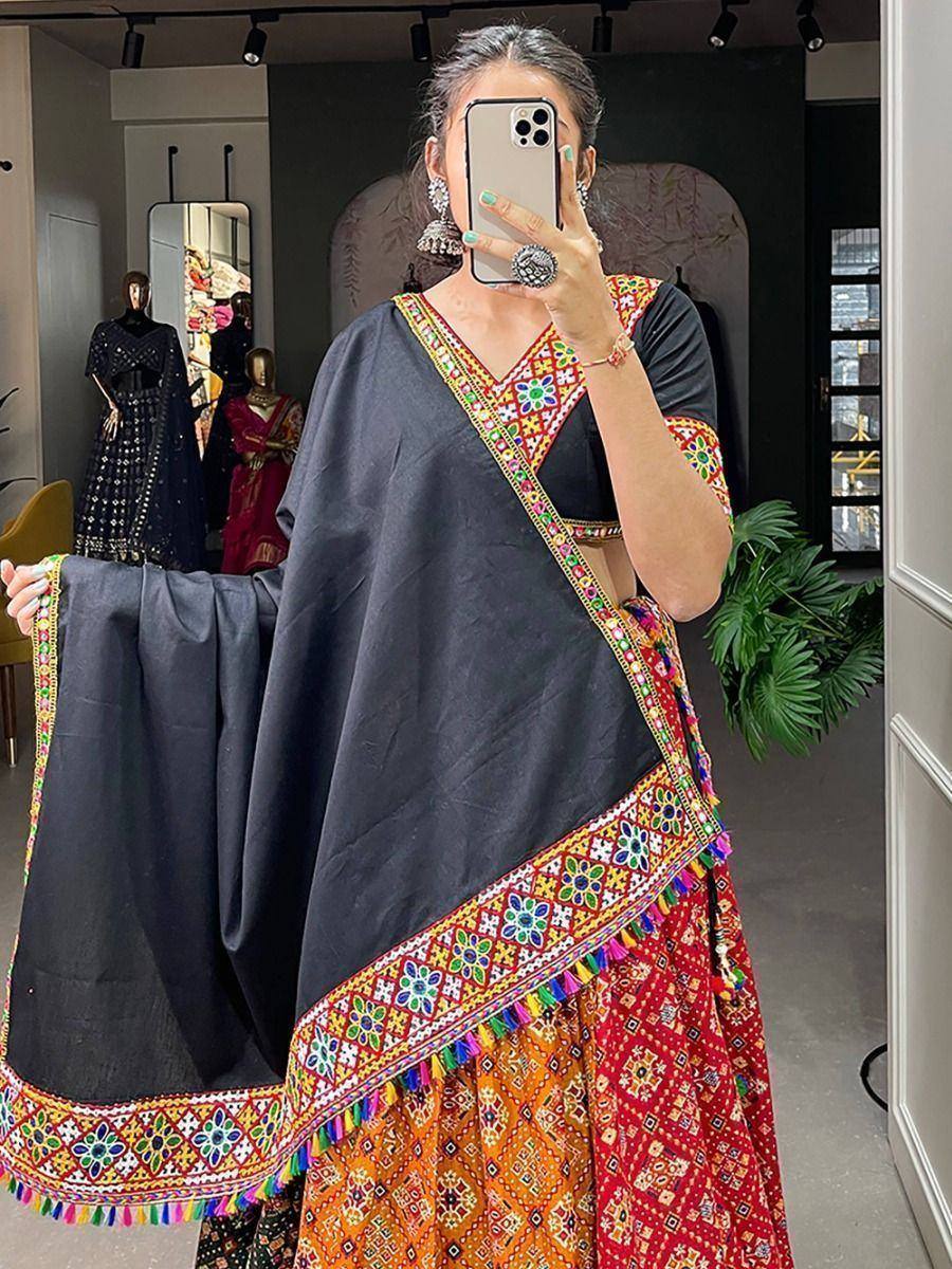 Woman wearing black and red embroidered lehenga choli with colorful mirror work and tassels, perfect for Indian ethnic occasions.