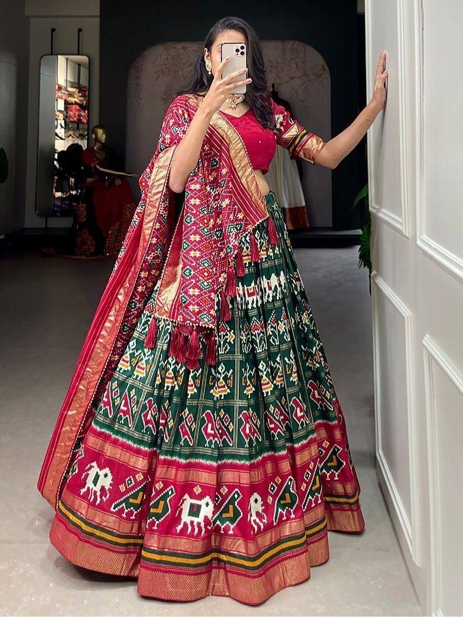 Woman in vibrant red and green printed lehenga choli with ethnic motifs, taking mirror selfie