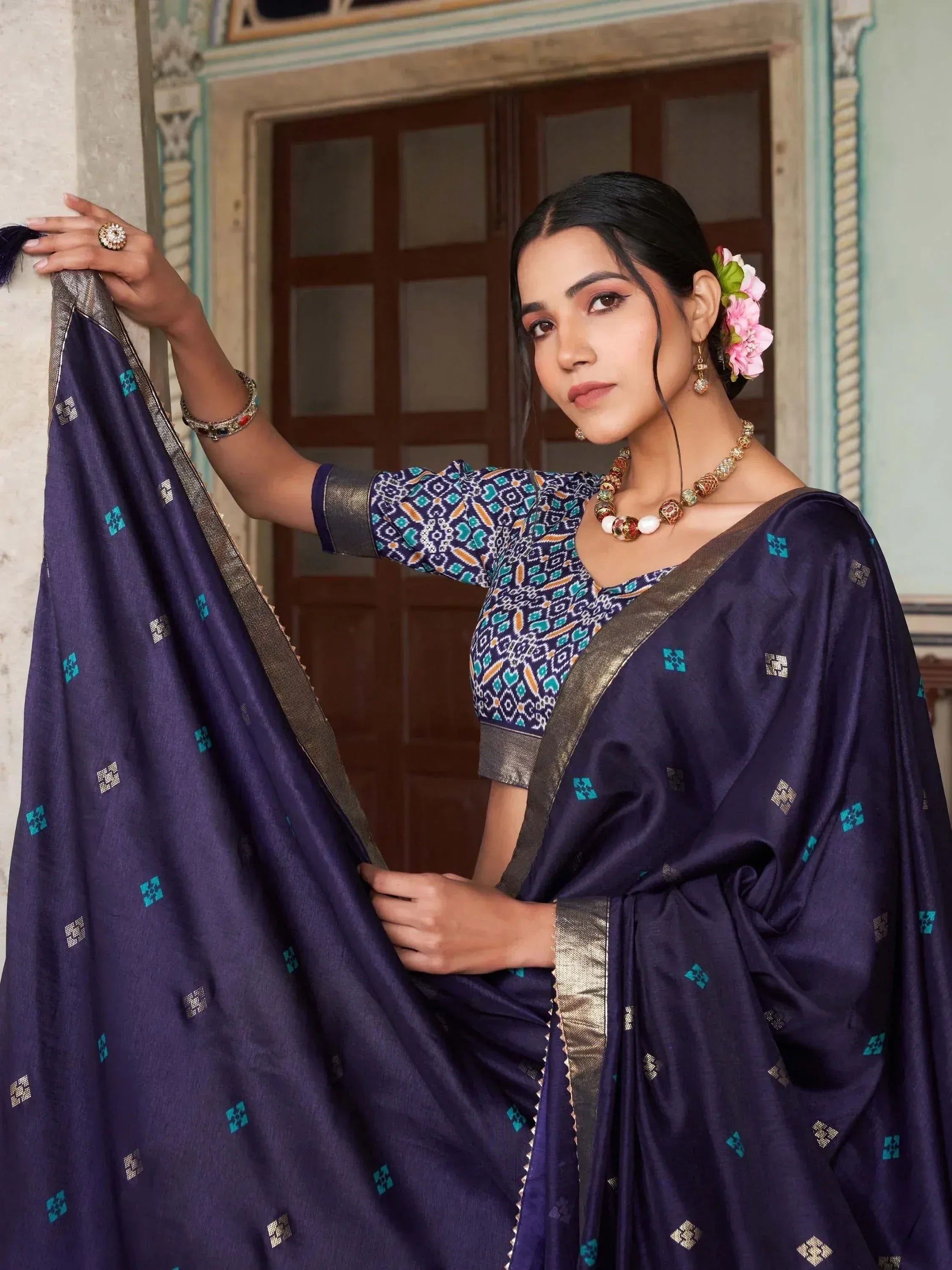 Woman in purple printed saree with gold border, floral hair accessory, traditional Indian ethnic wear