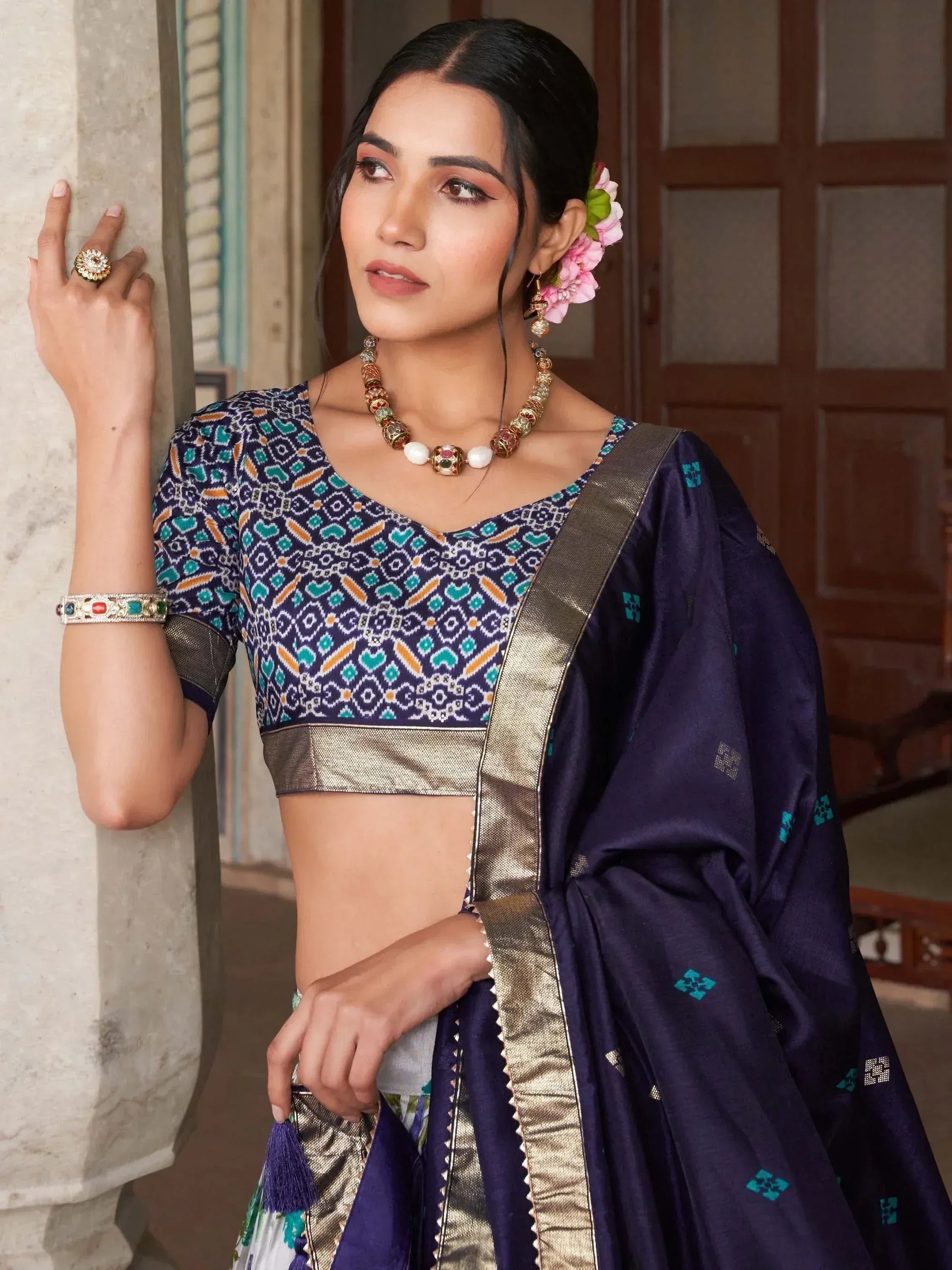Woman in navy blue printed saree with gold border and matching blouse, styled with floral hair accessory and traditional jewelry.