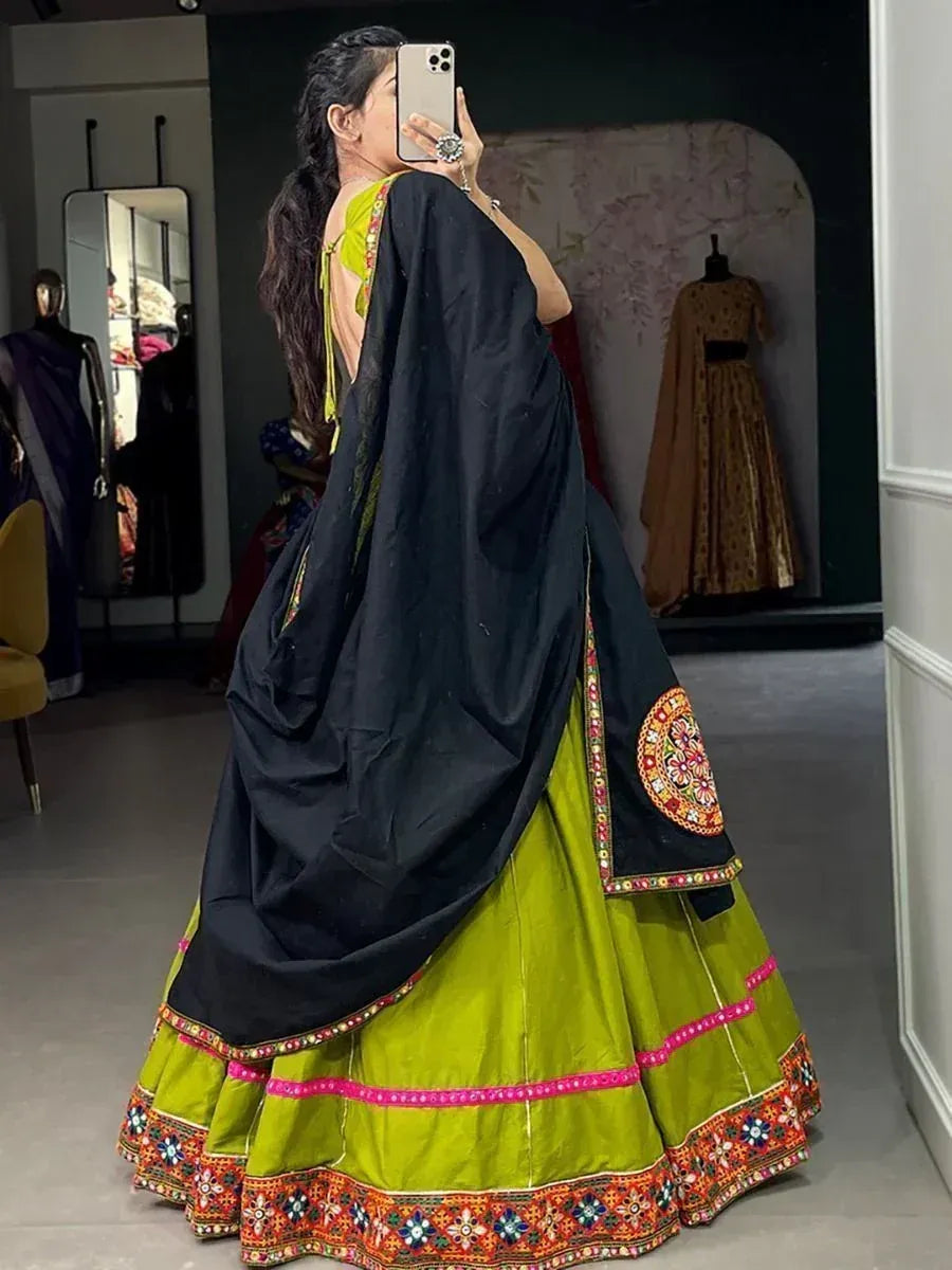 Woman in vibrant green lehenga with black dupatta, colorful embroidery, taking mirror selfie in boutique