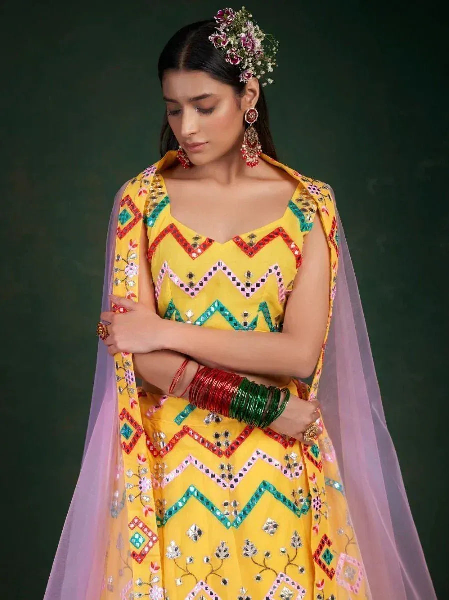 Yellow ethnic lehenga choli with mirror work, floral hair accessory, and colorful bangles