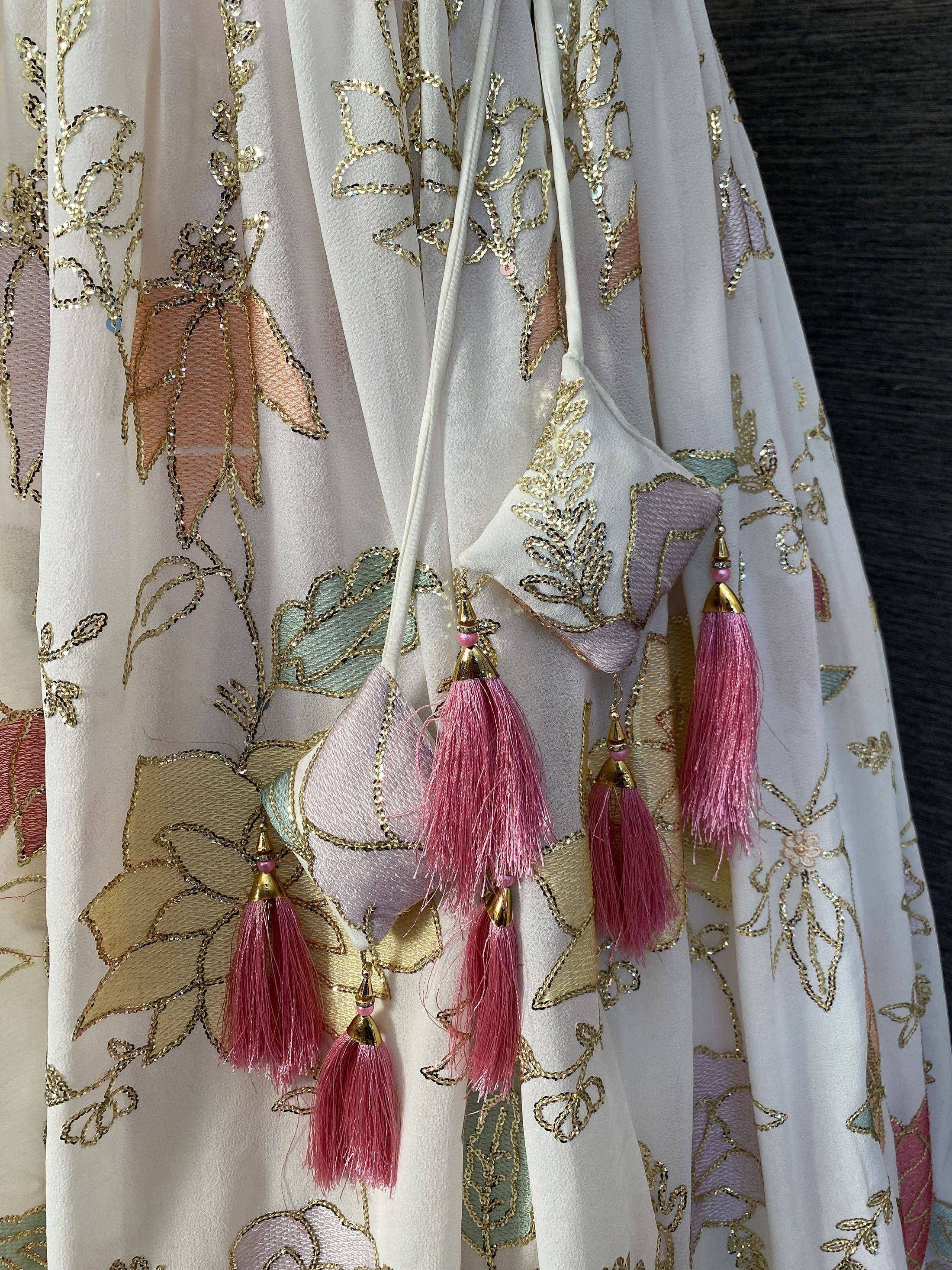 White ethnic gown with gold sequin floral embroidery and pink tassels, perfect for Indian occasions.