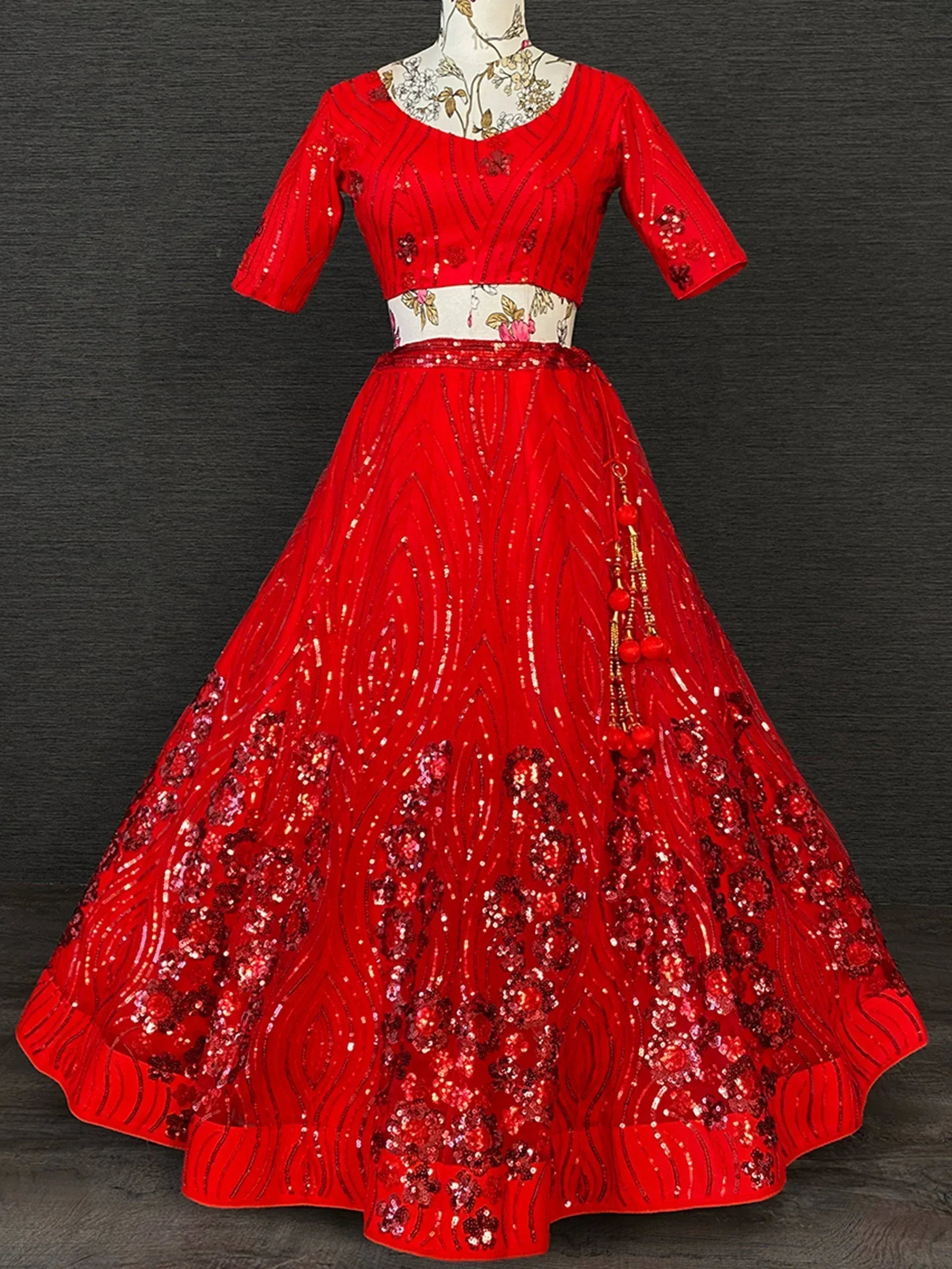 Red sequined lehenga choli with floral embroidery and pom-pom tassels, perfect for Indian ethnic wear occasions.
