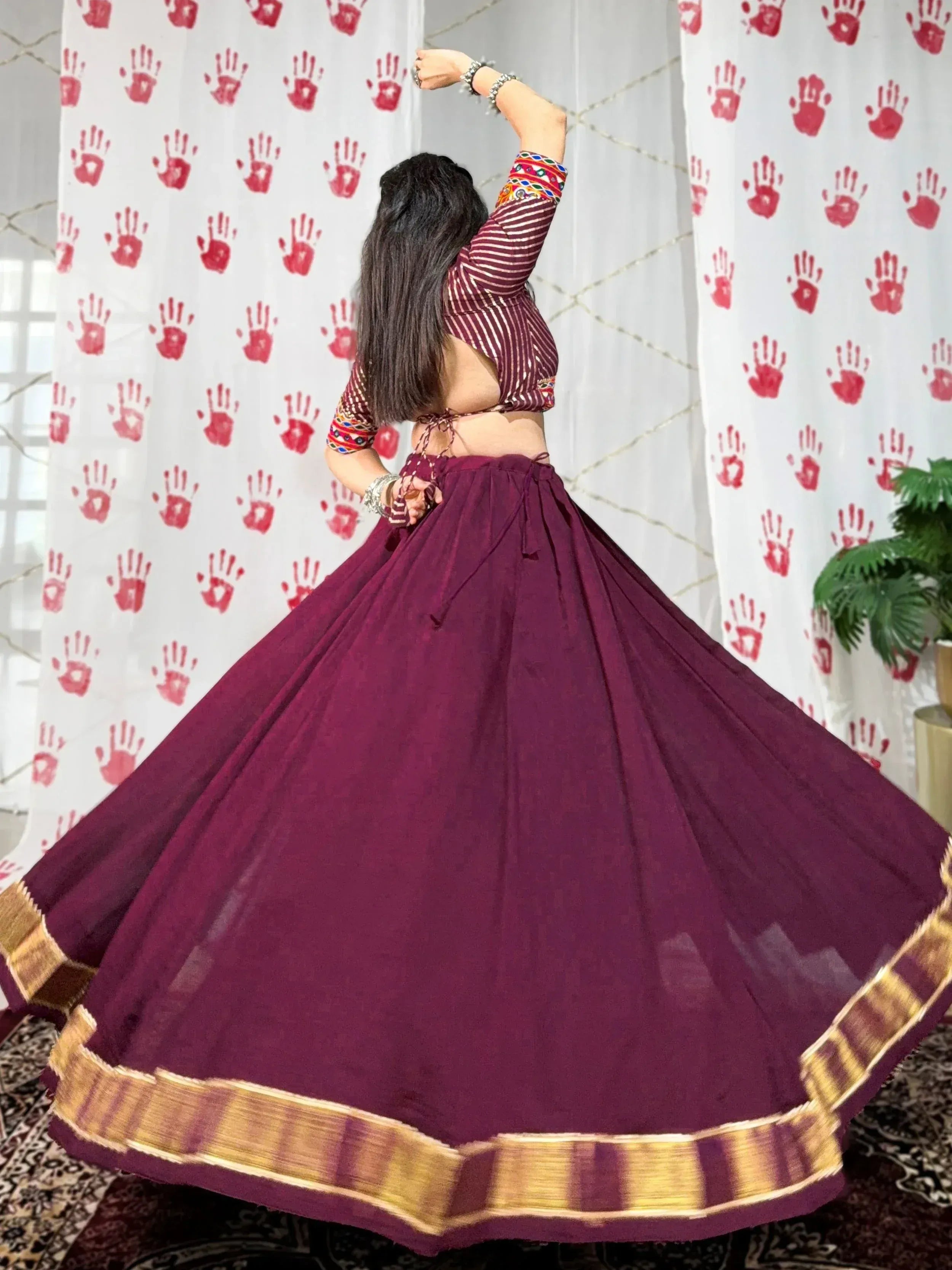 Woman twirling in maroon ethnic lehenga choli with striped blouse and gold border, perfect for Indian celebrations
