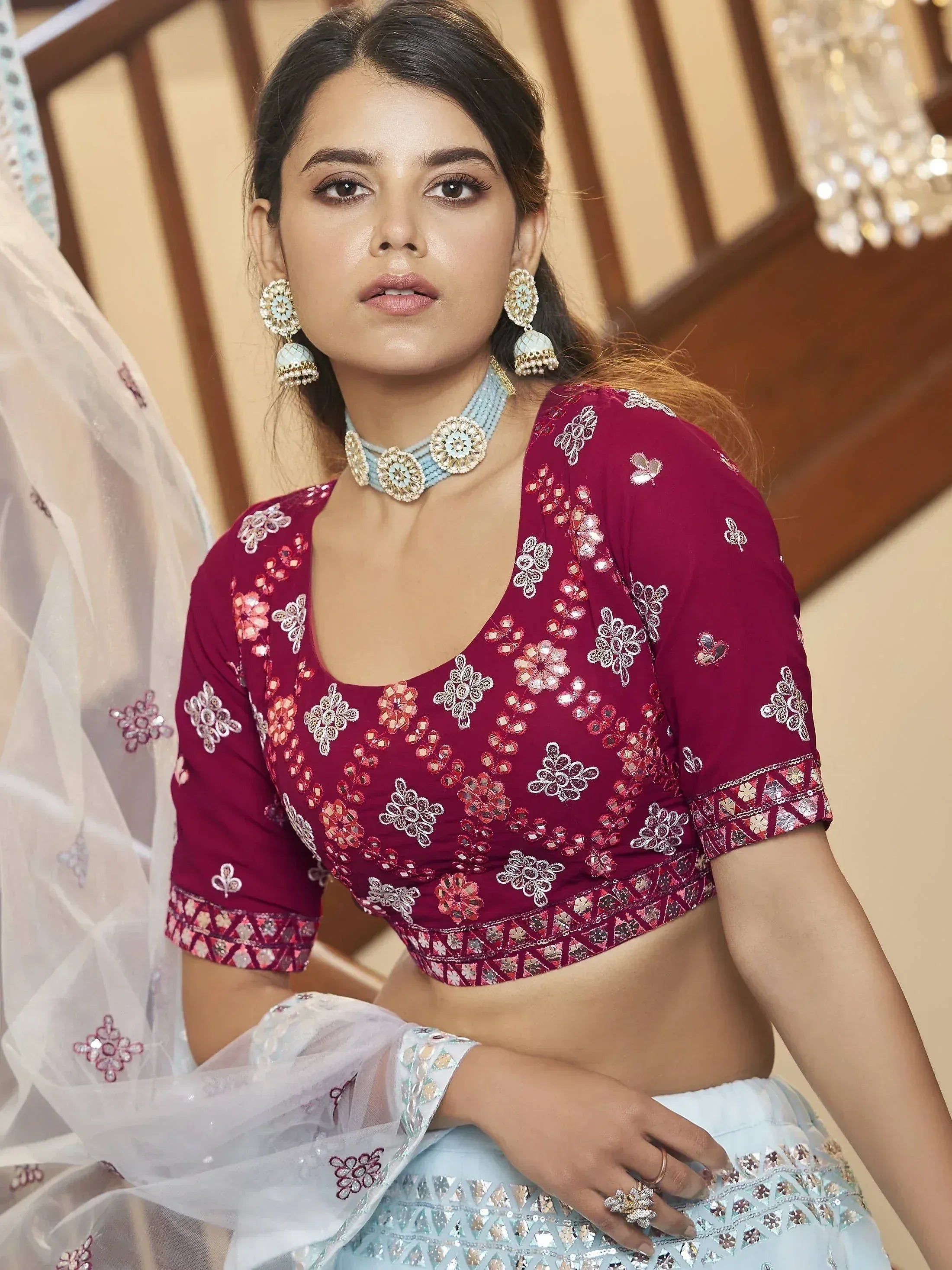 Maroon embroidered blouse with floral sequin work, paired with light blue lehenga and traditional jewelry
