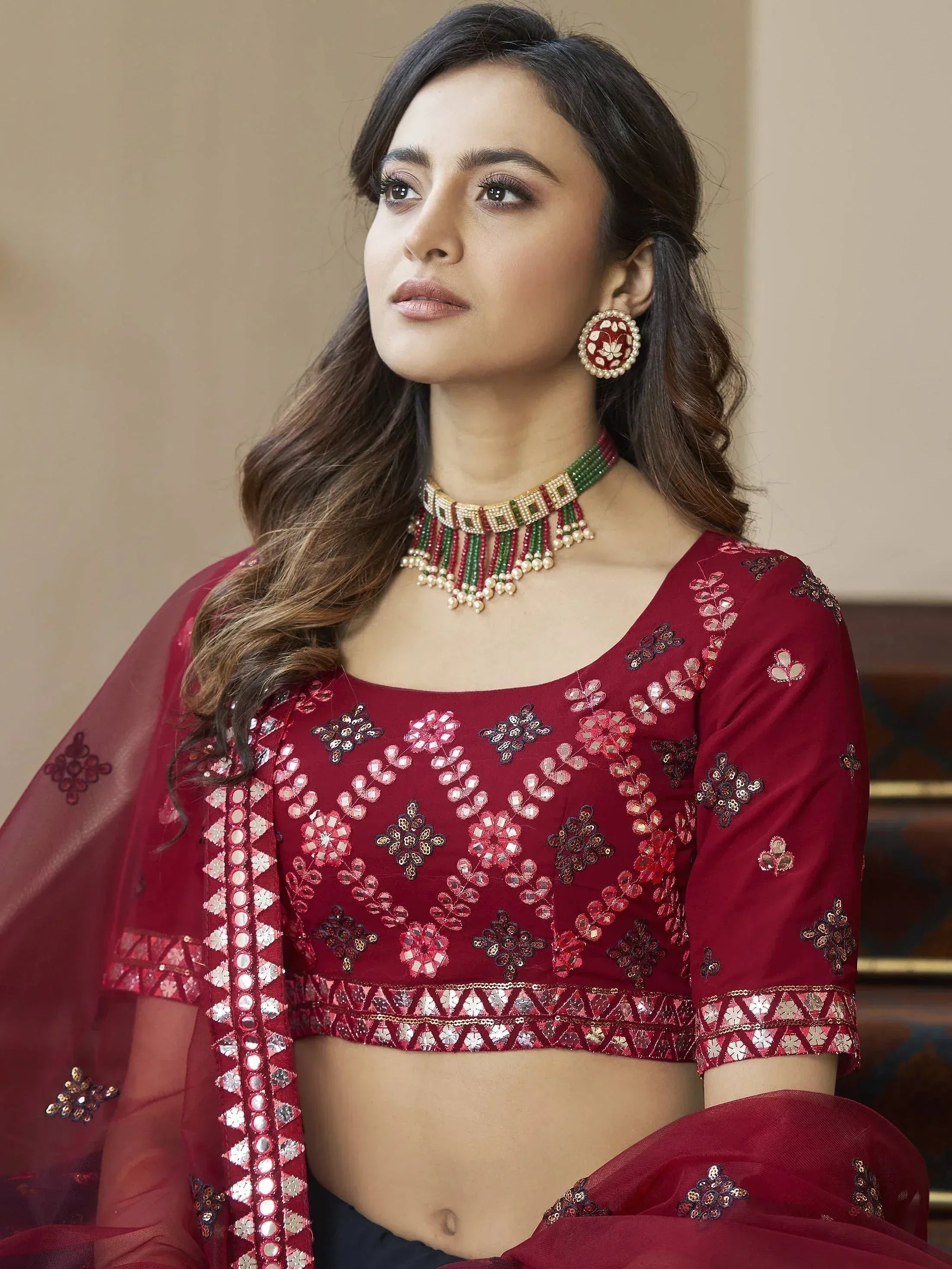 Maroon embroidered lehenga choli with mirror work, paired with traditional jewelry for Indian ethnic wear