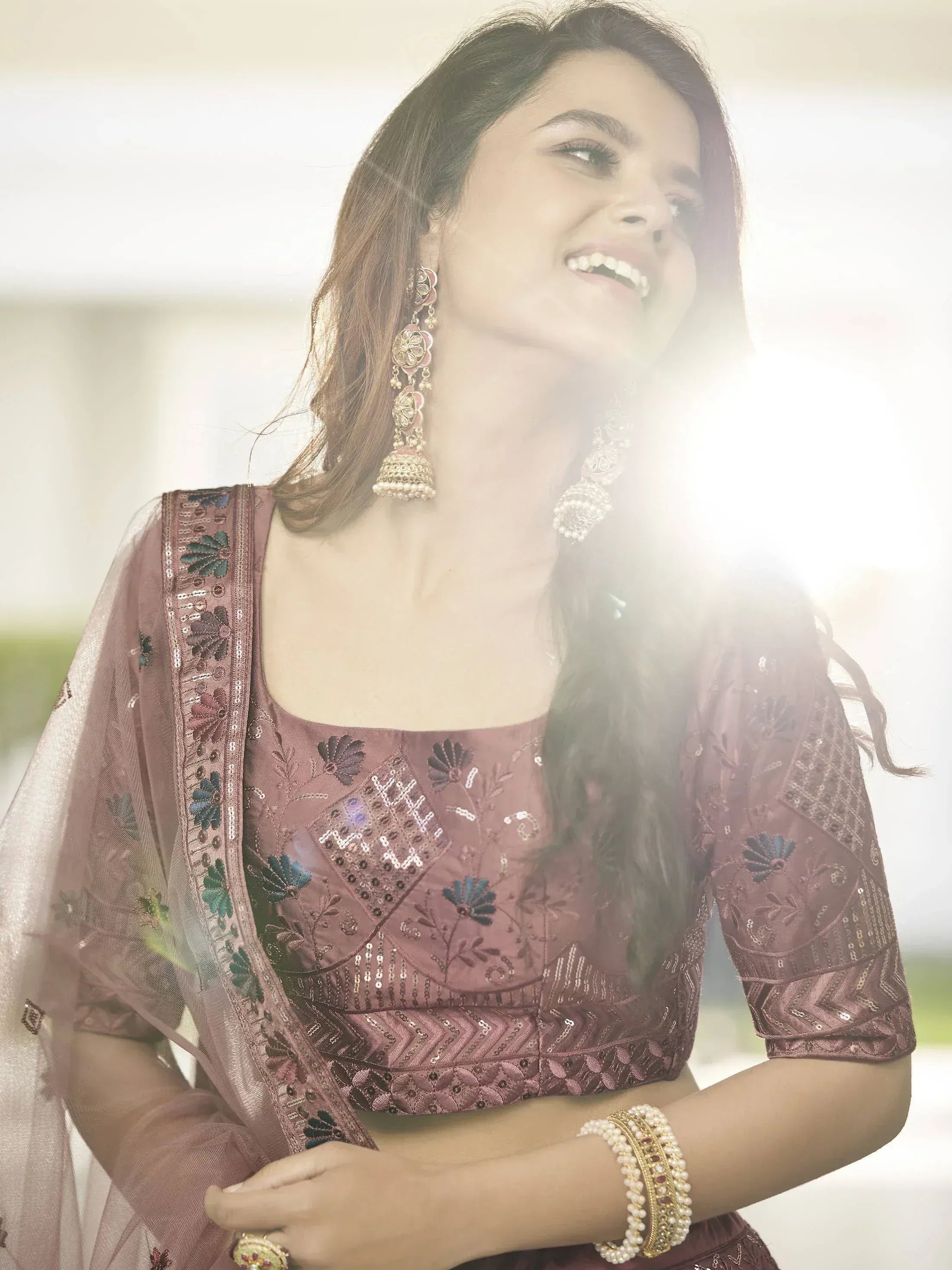 Woman in embroidered mauve lehenga choli with floral sequin work, jhumka earrings, and pearl bangles