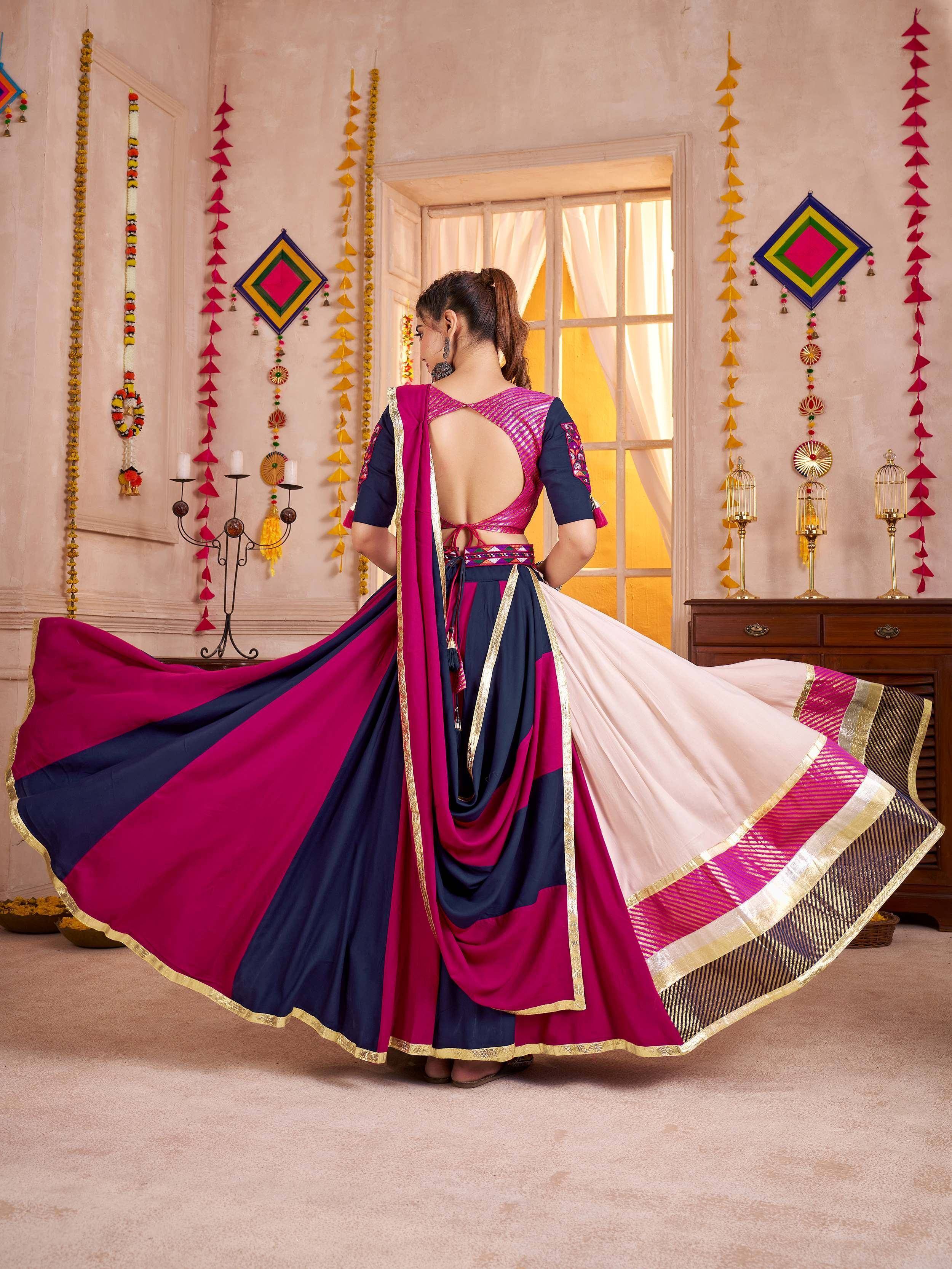 Woman in vibrant pink and navy blue lehenga choli with gold trim, twirling in festive Indian decor