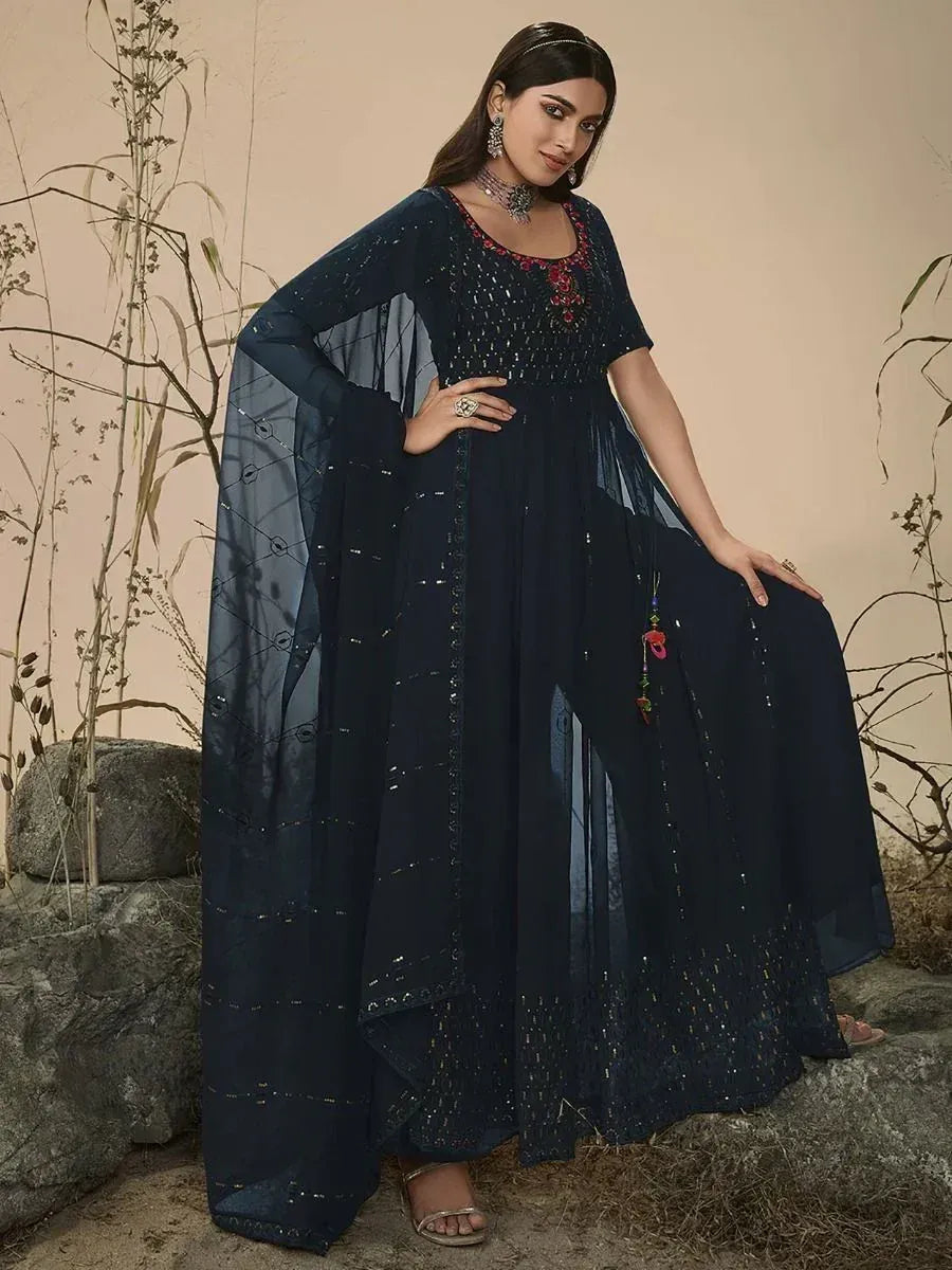Woman wearing navy blue embroidered ethnic gown with sheer cape sleeves, standing outdoors