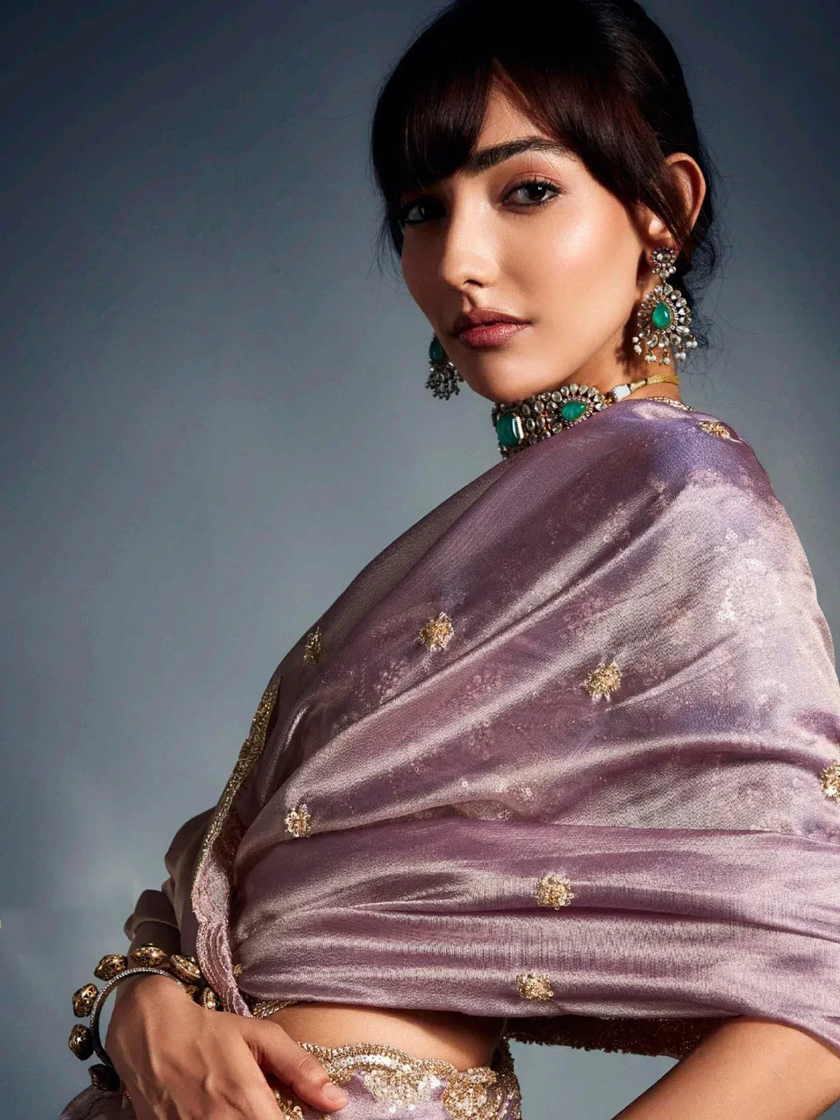 Elegant woman in purple velvet saree with gold embroidery and emerald jewelry, showcasing Indian ethnic wear.