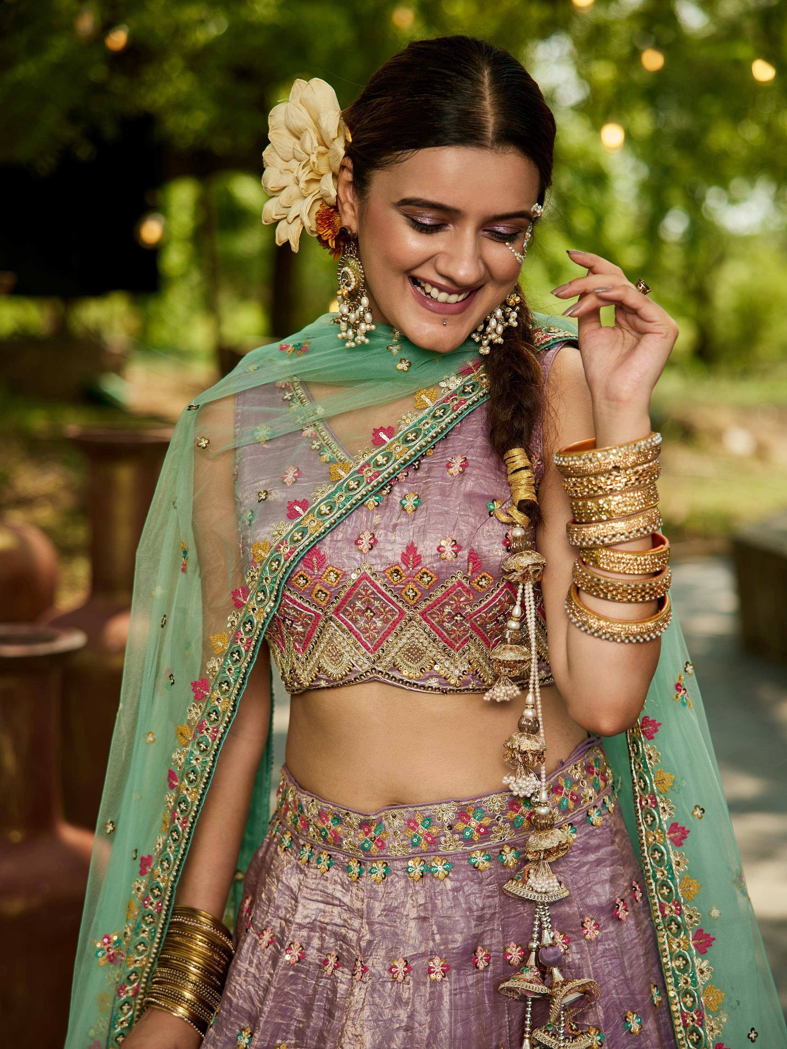 Woman in purple embroidered lehenga choli with green dupatta, gold jewelry, and floral hair accessory
