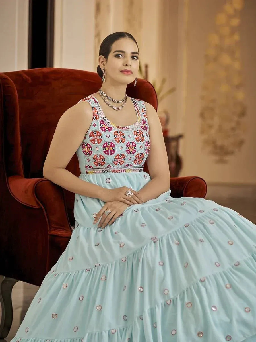 Woman in light blue embroidered ethnic gown with mirror work, seated on velvet chair