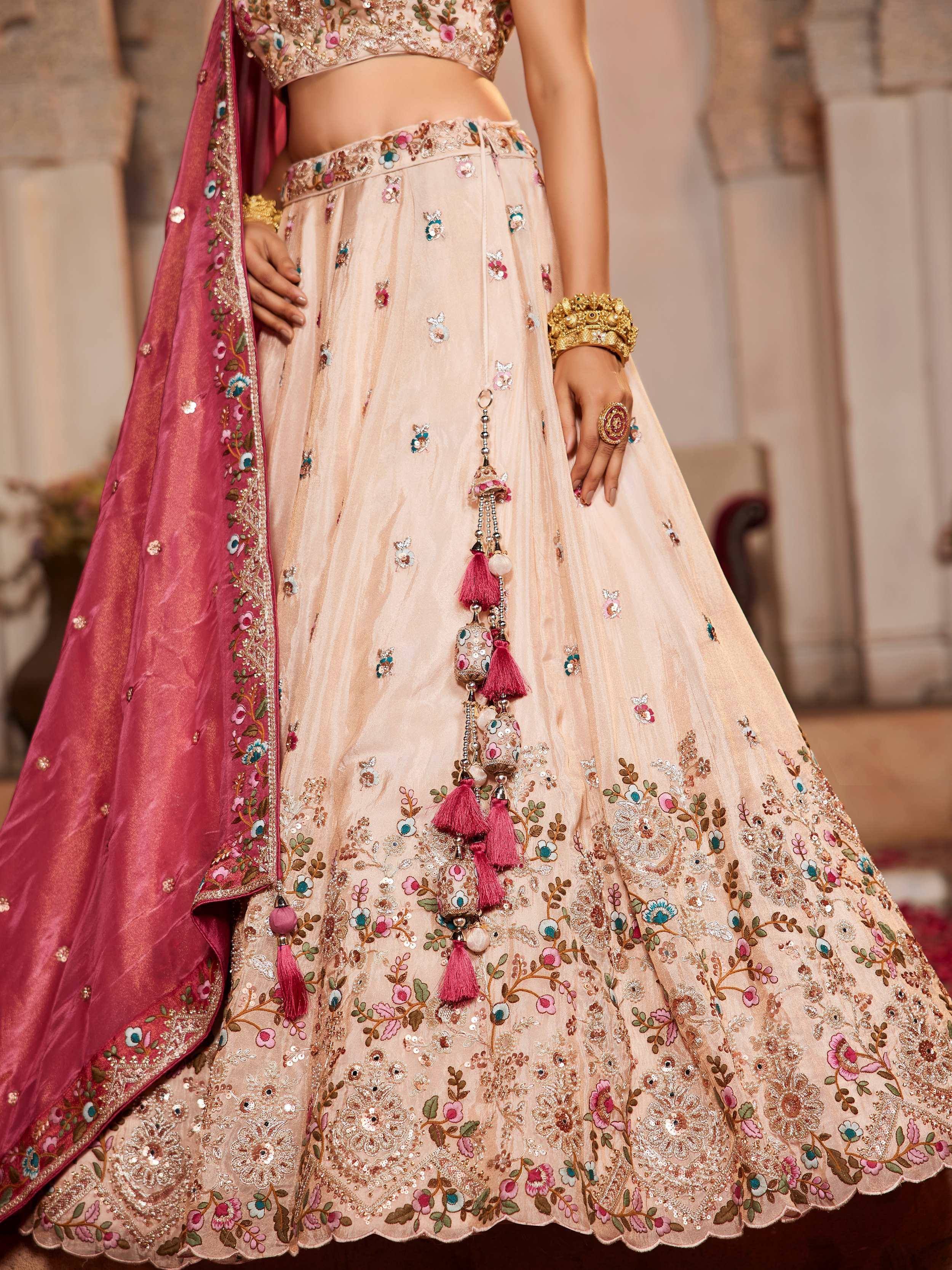 Elegant beige lehenga choli with floral embroidery, pink dupatta, and tassels for Indian weddings